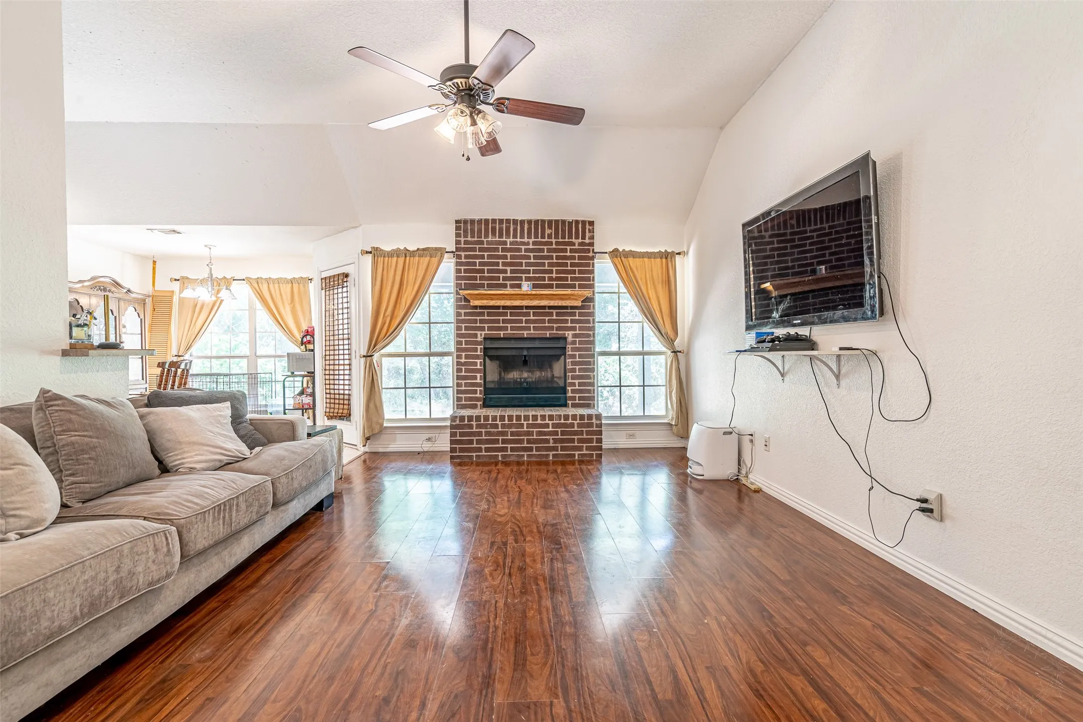 Spacious living area featuring wood-finish flooring, a vaulted ceiling, and a ceiling fan