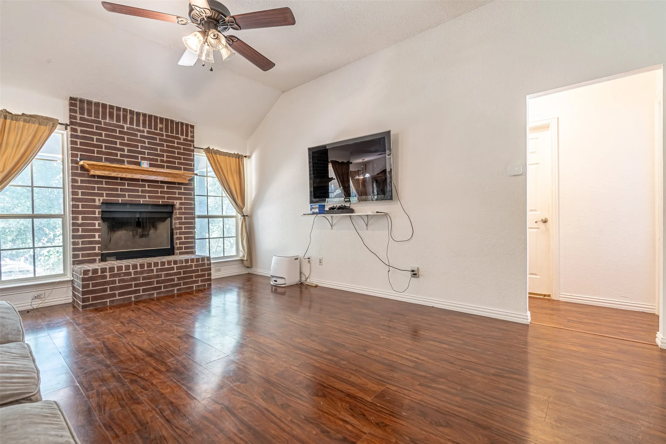 Spacious living area featuring high vaulted ceilings, wood-finish flooring, and a red brick fireplace with a wood mantel