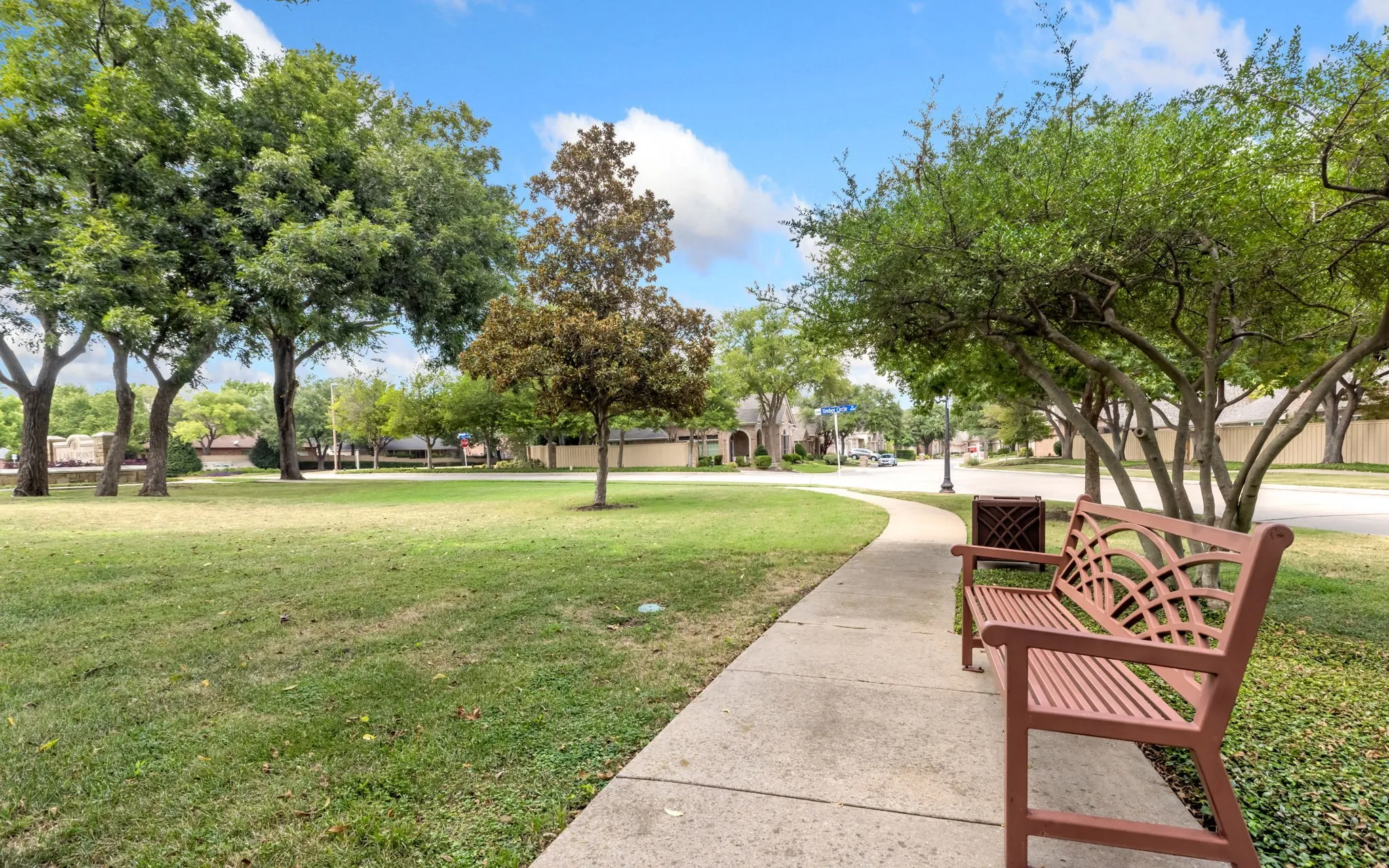 Serene park setting with mature shade trees, manicured lawn, and concrete pedestrian pathways
