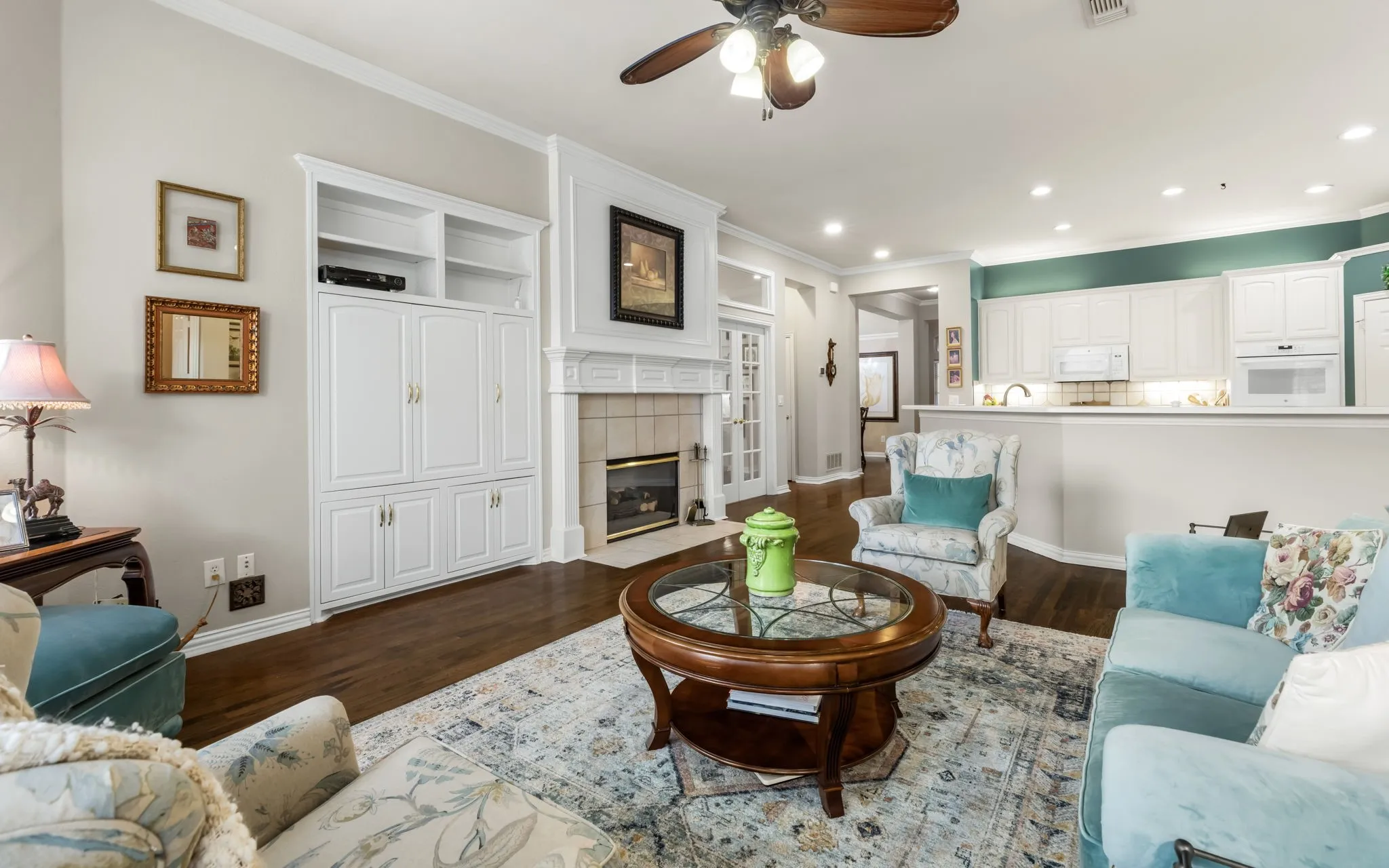 Hardwood flooring, crown molding, built-in cabinetry, tiled fireplace surround, and a ceiling fan