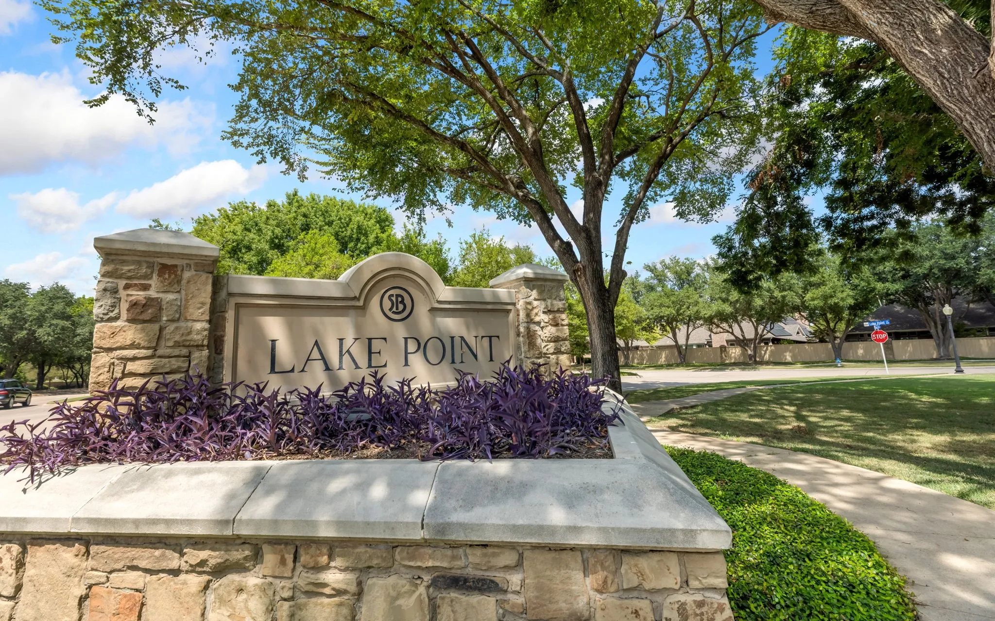 Stone monument sign with raised lettering, surrounded by established landscaping and mature trees