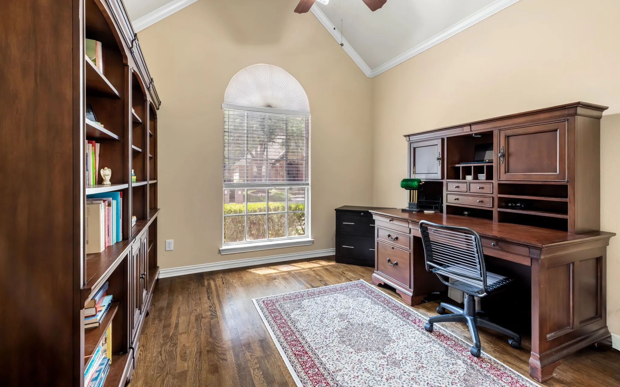 Vaulted ceiling with crown molding, arched window, wood-finish flooring, and built-in shelving