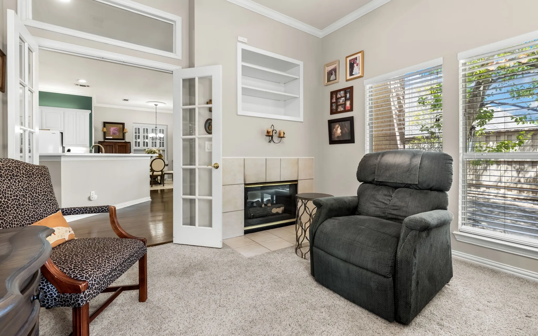 Recessed fireplace with tile surround, built-in shelving, two large windows, and double French doors with transom