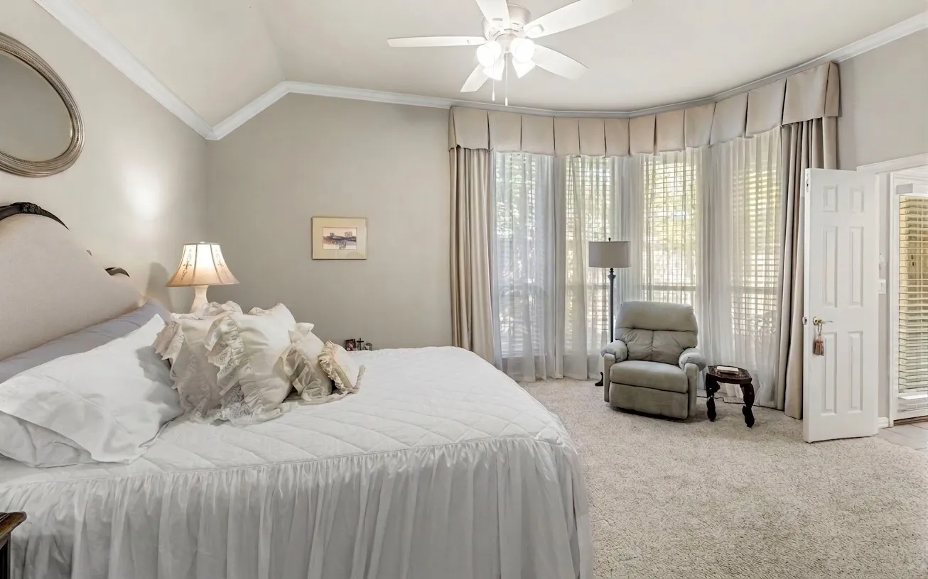 Vaulted ceiling with crown molding, ceiling fan, curved bay window with blinds and draperies, and neutral carpeting