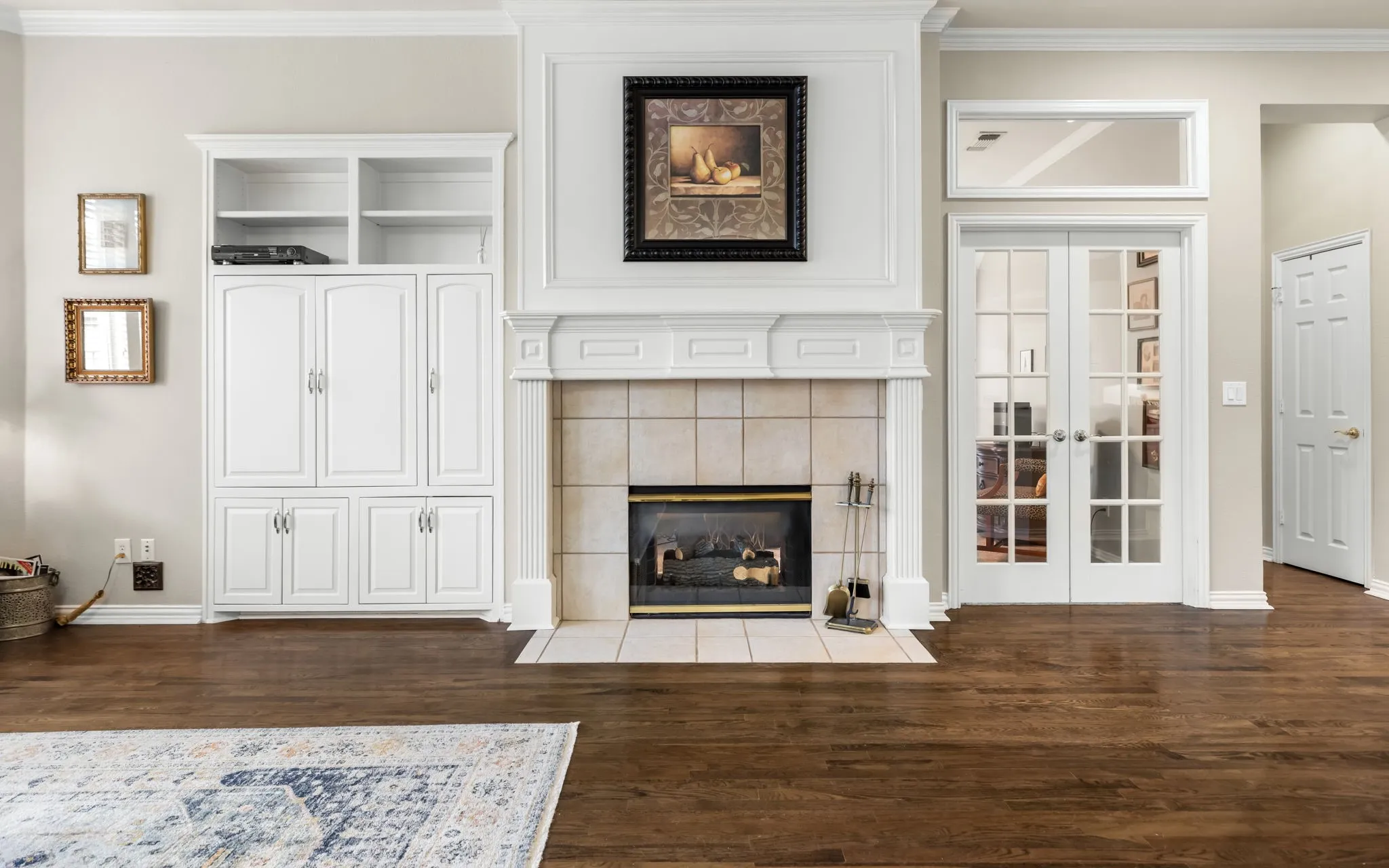 Hardwood flooring with a tile-surround fireplace, detailed mantel, built-in cabinetry, and double French doors