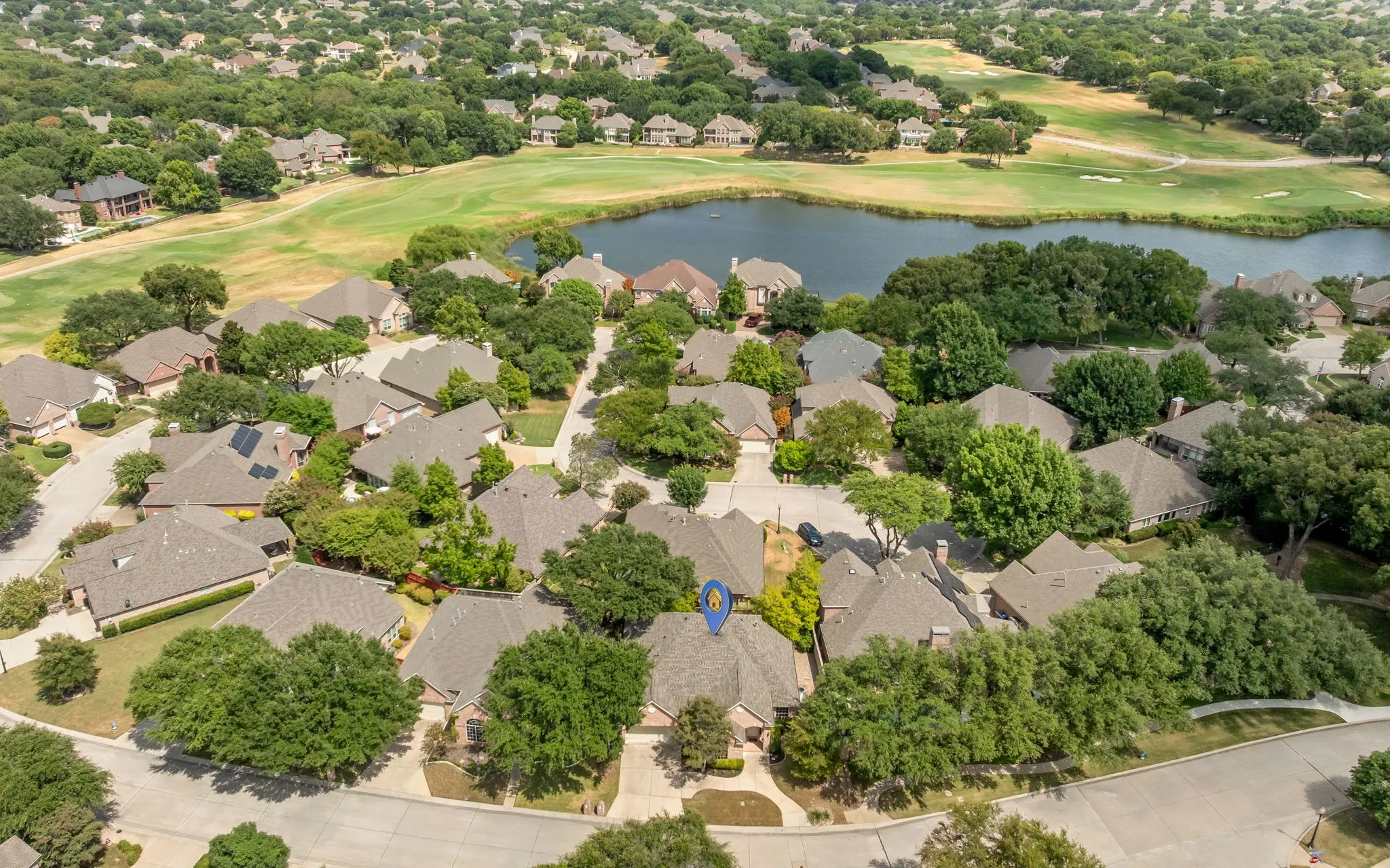 Residential community with mature tree canopies, featuring a lake and golf course in the background