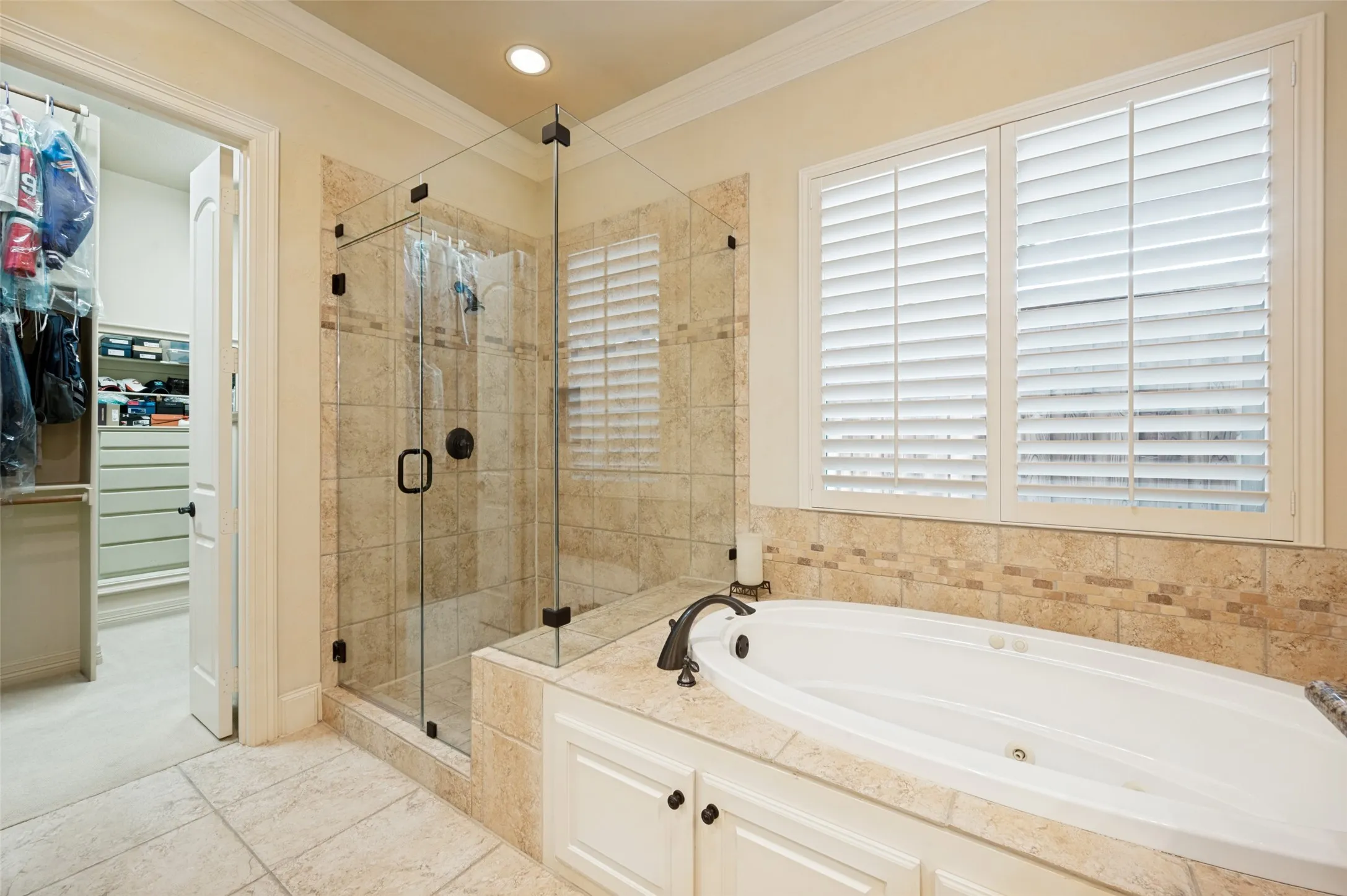 Spacious bathroom featuring a glass-enclosed shower, built-in soaking tub with tile surround, and plantation shutters