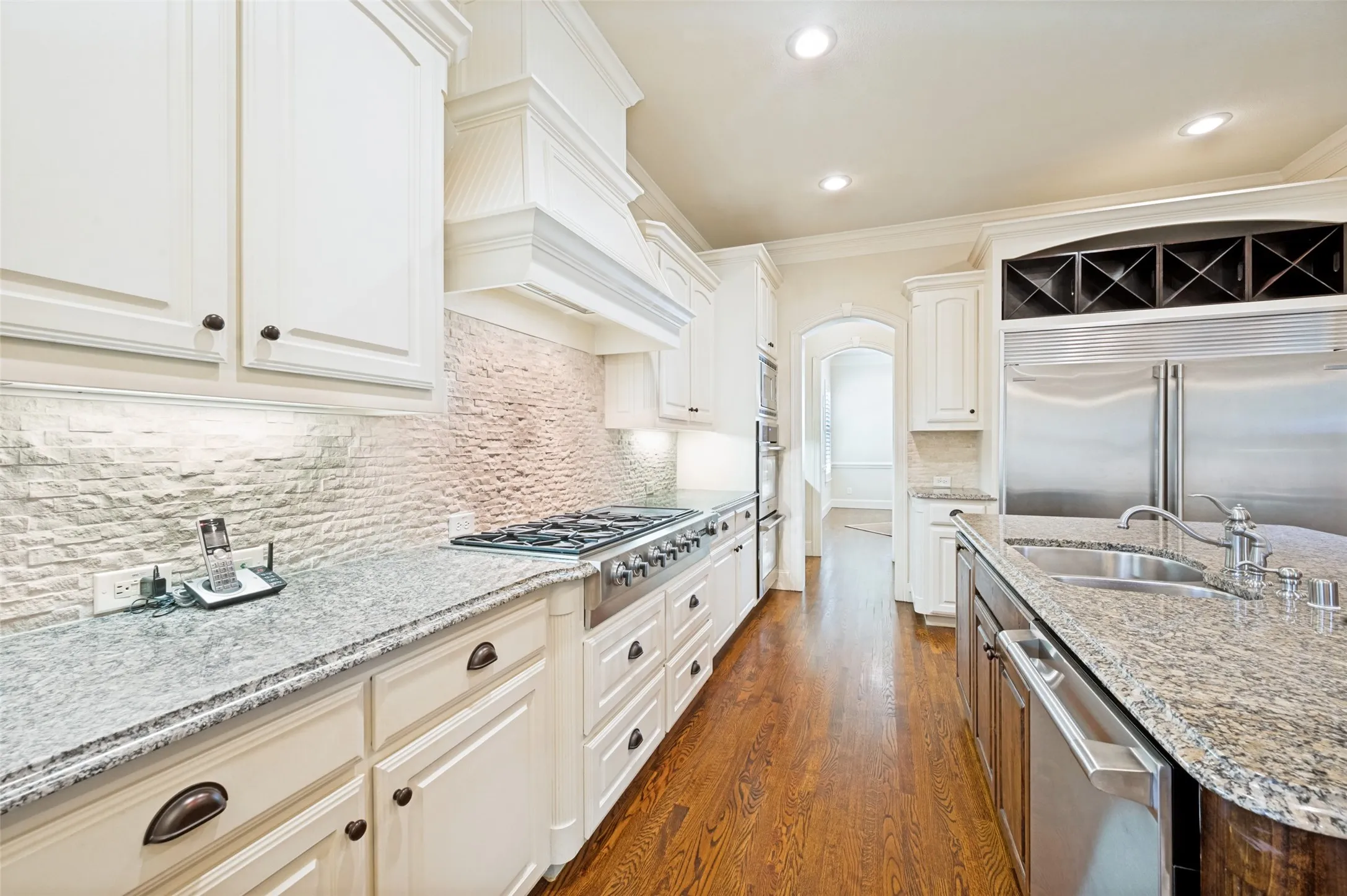 Gourmet kitchen featuring white cabinetry, a stone tile backsplash, a professional-grade range, a built-in wine rack, and extensive countertop space