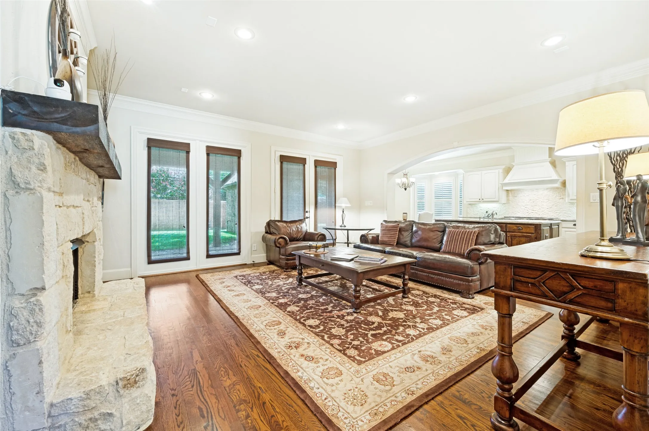 Spacious living area featuring wood-finish flooring, a stone fireplace with a substantial wood mantel, recessed lighting, and multiple windows