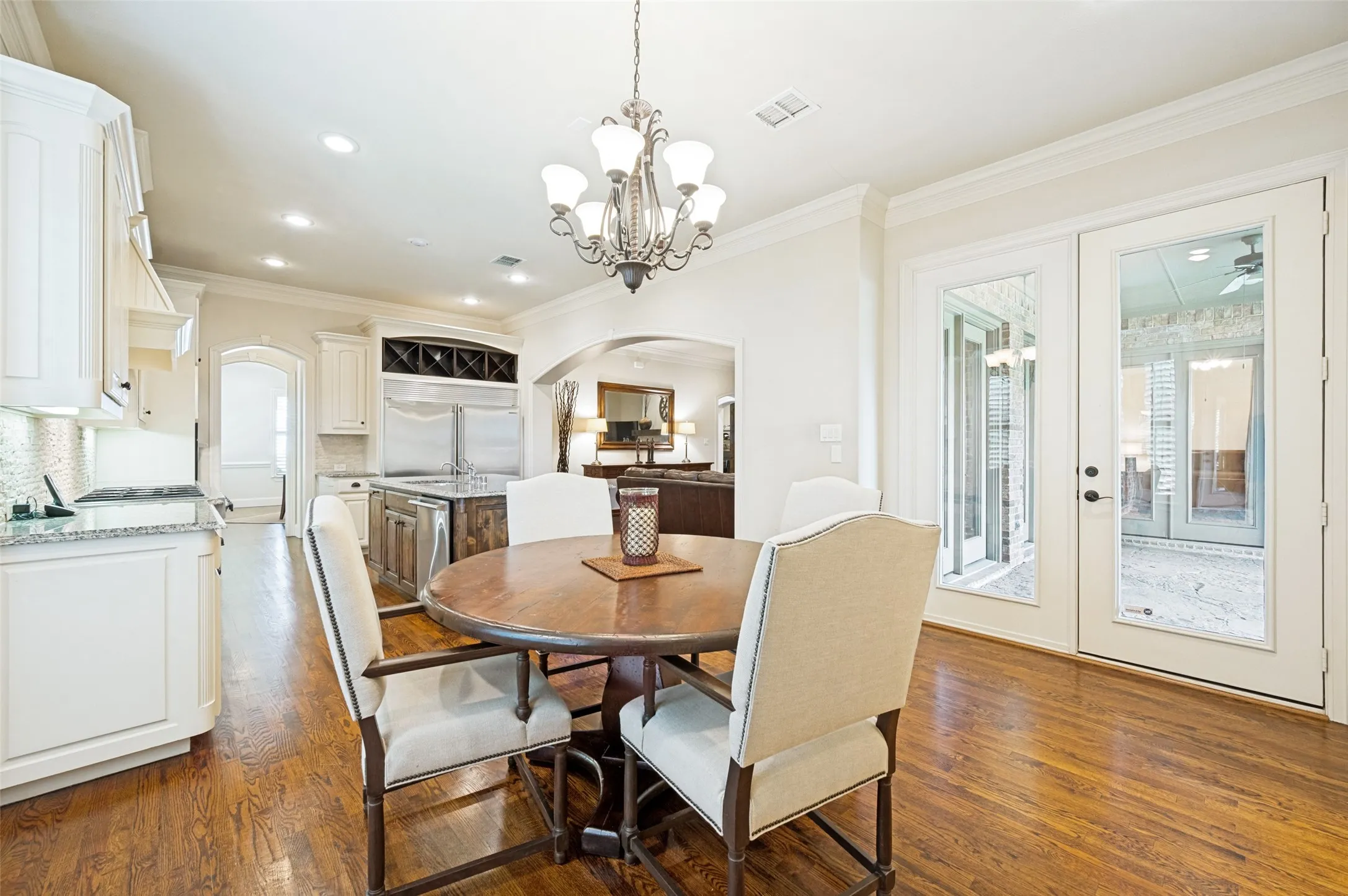 Gourmet kitchen and dining area featuring rich wood-finish flooring, white cabinetry, granite countertops, and stainless steel appliances