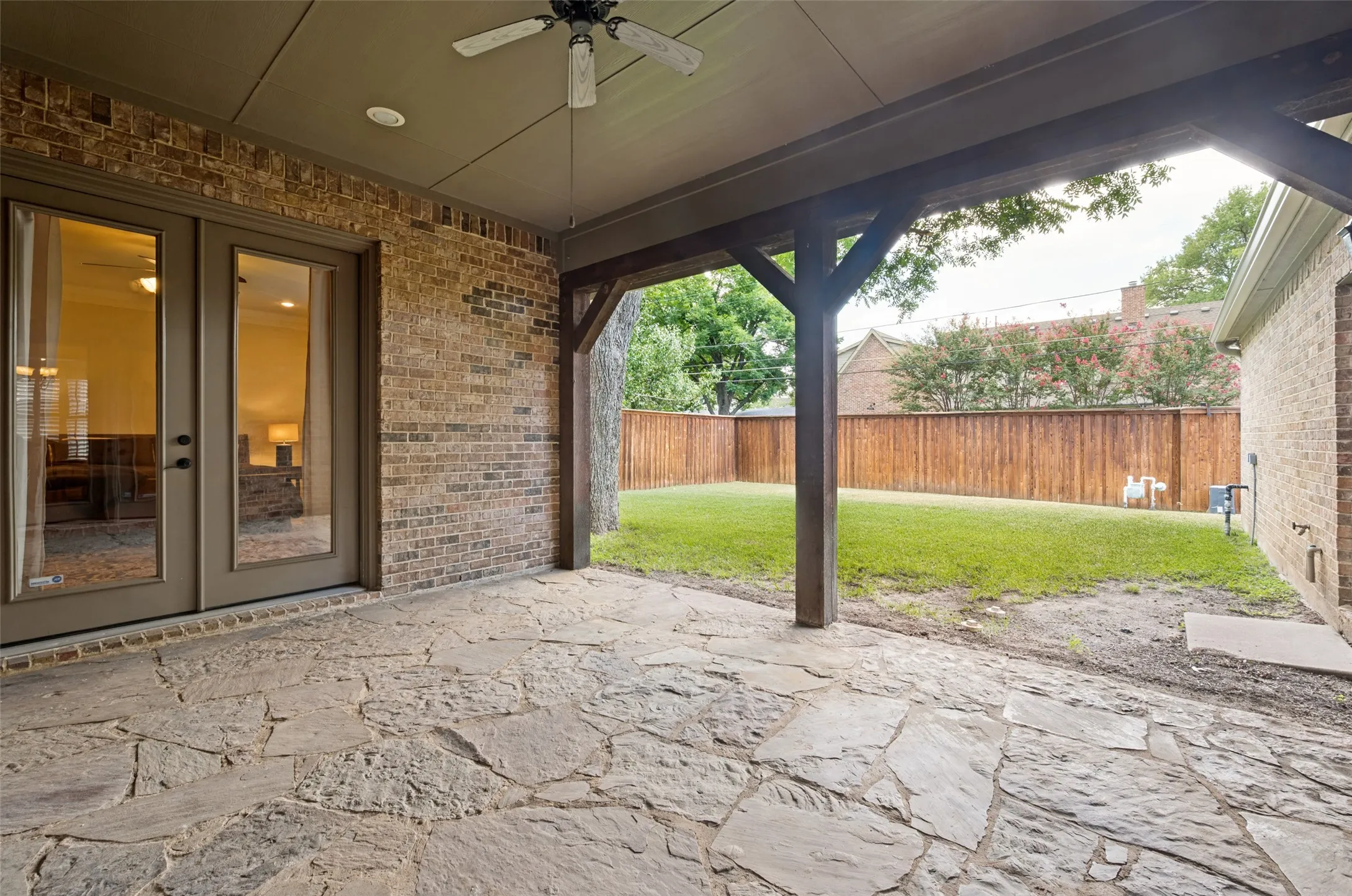 Covered patio featuring flagstone flooring, brick exterior, and wood-toned support beams