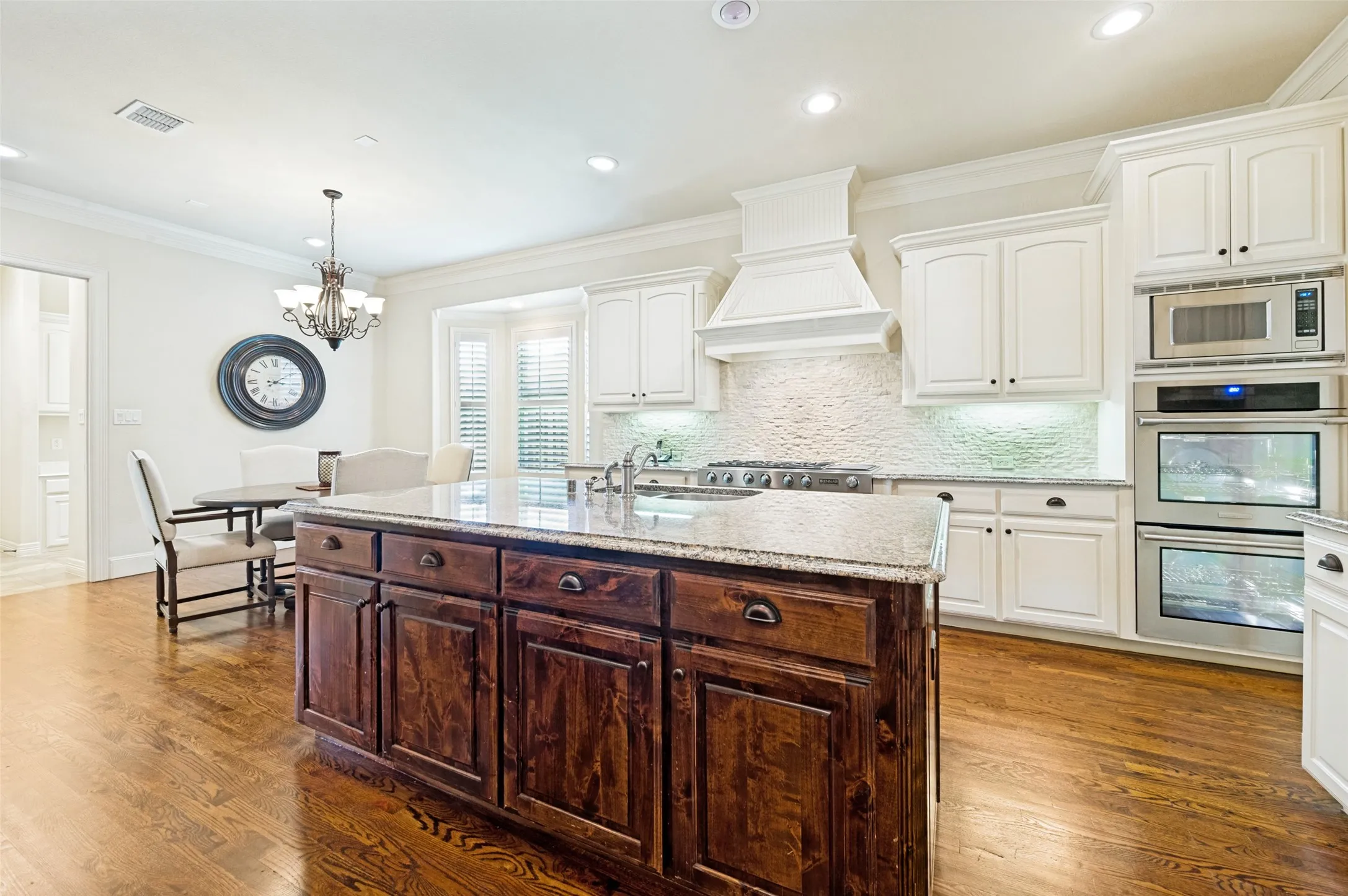 Kitchen featuring a substantial wood-finish island with a stone countertop, white cabinetry, integrated stainless steel appliances, and wood-finish flooring