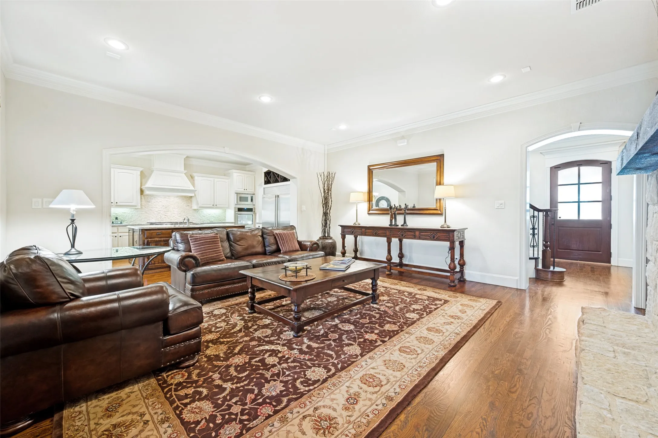 Hardwood flooring extends throughout this space, featuring an arched entryway to the kitchen with white cabinetry and a built-in range hood