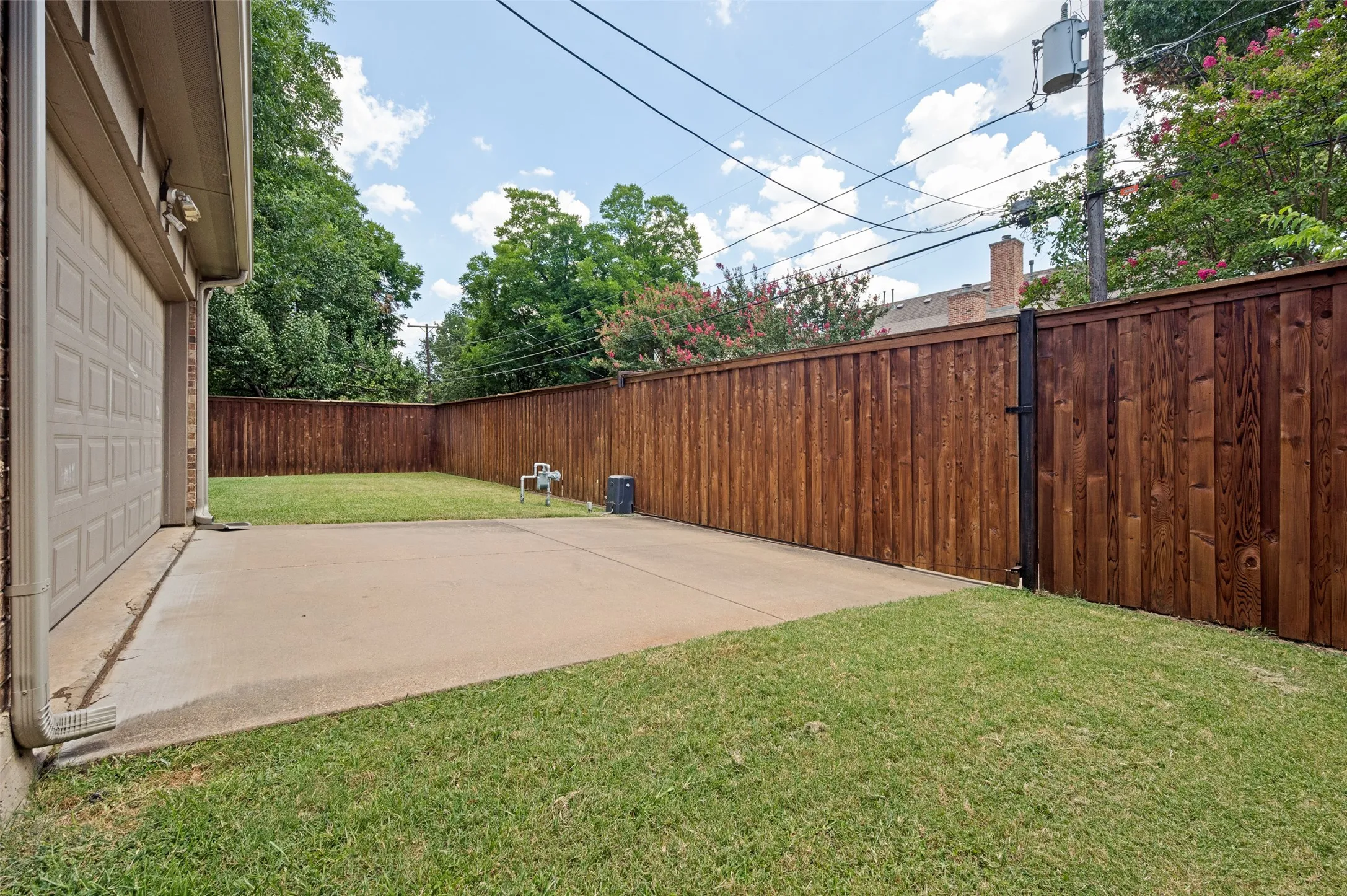 Expansive backyard featuring a stained wood privacy fence, concrete patio, and a manicured lawn