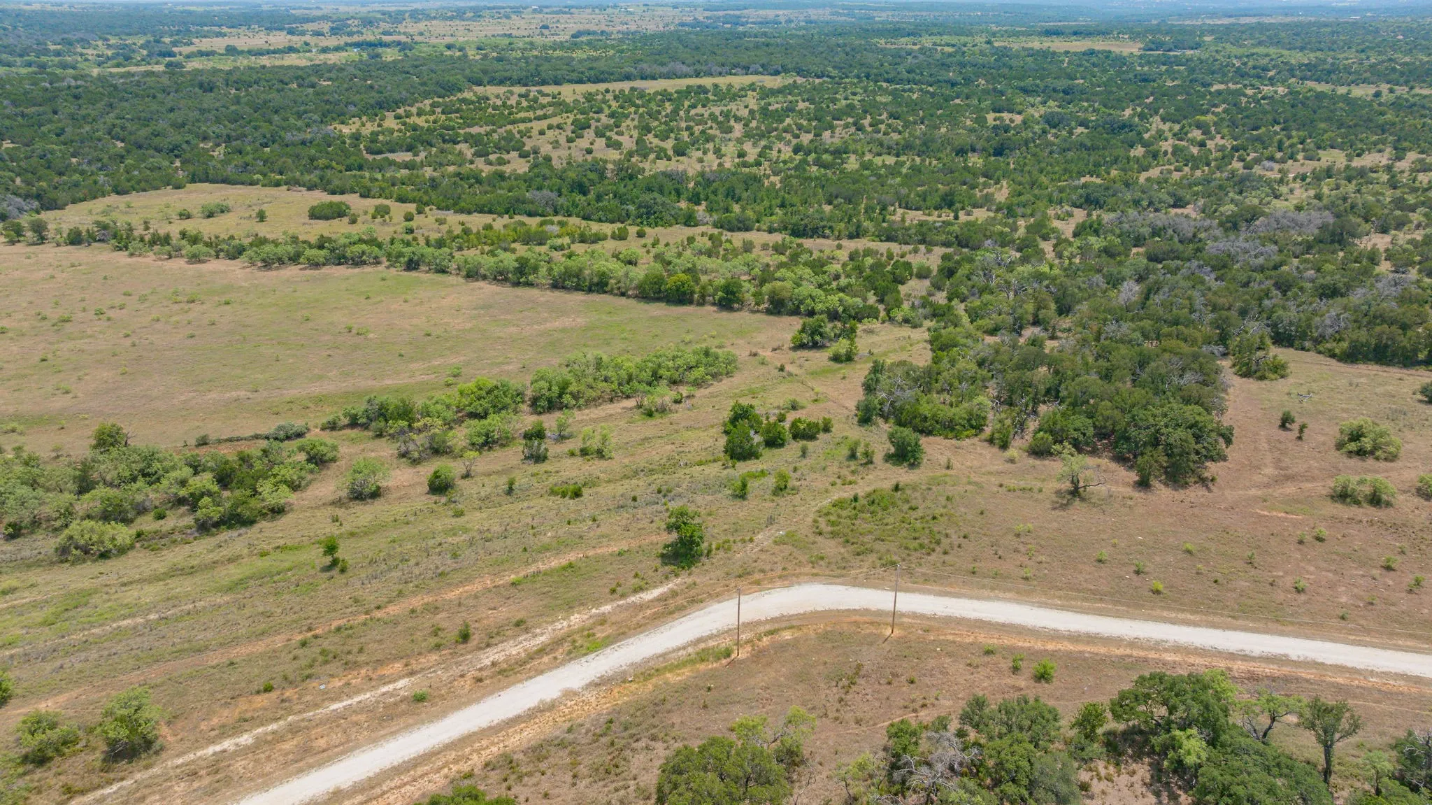 Expansive rural acreage featuring rolling pastureland with scattered mature trees and a newly paved access road