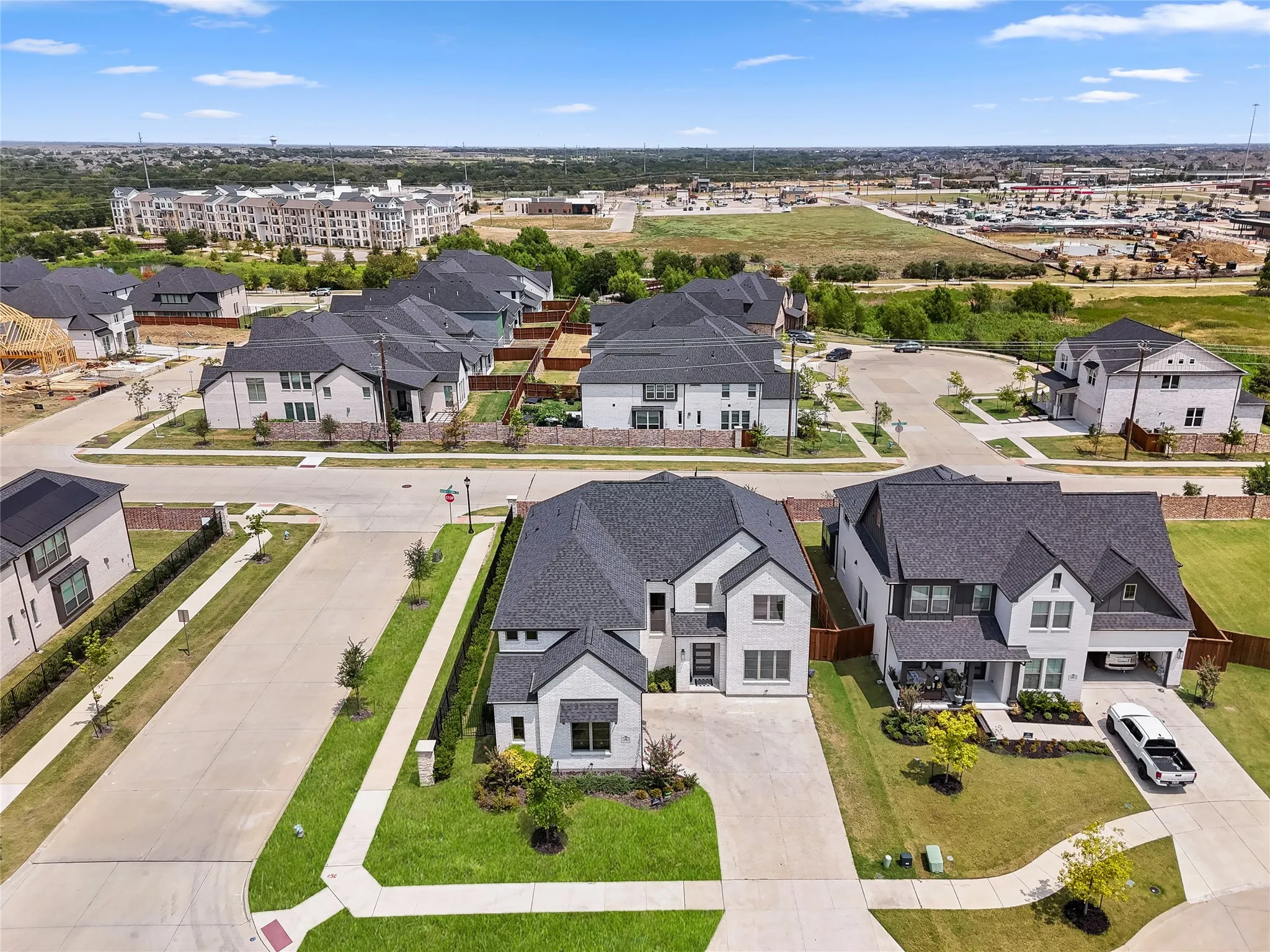Aerial view showcasing a newly constructed residential community with modern two-story homes featuring dark architectural rooflines, manicured lawns, and concrete driveways