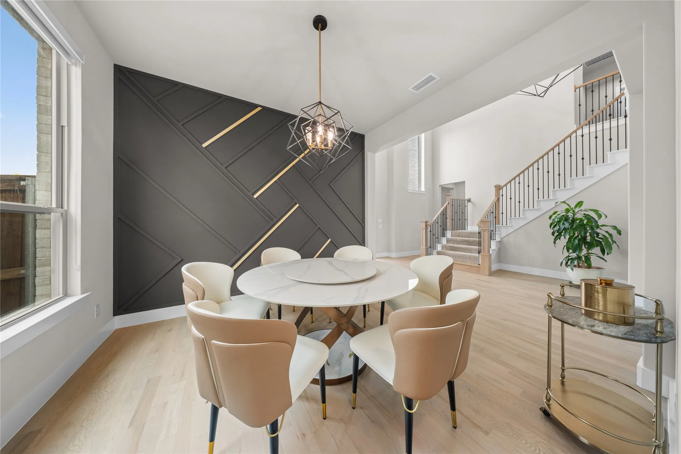Decorative accent wall with integrated lighting, wood-finish flooring, staircase with dark metal spindles and wood handrail, and a contemporary chandelier