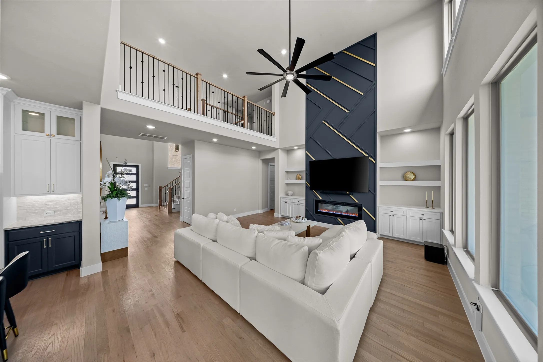 Open-concept living space anchored by a two-story ceiling and modern ceiling fan, featuring wood-finish flooring throughout