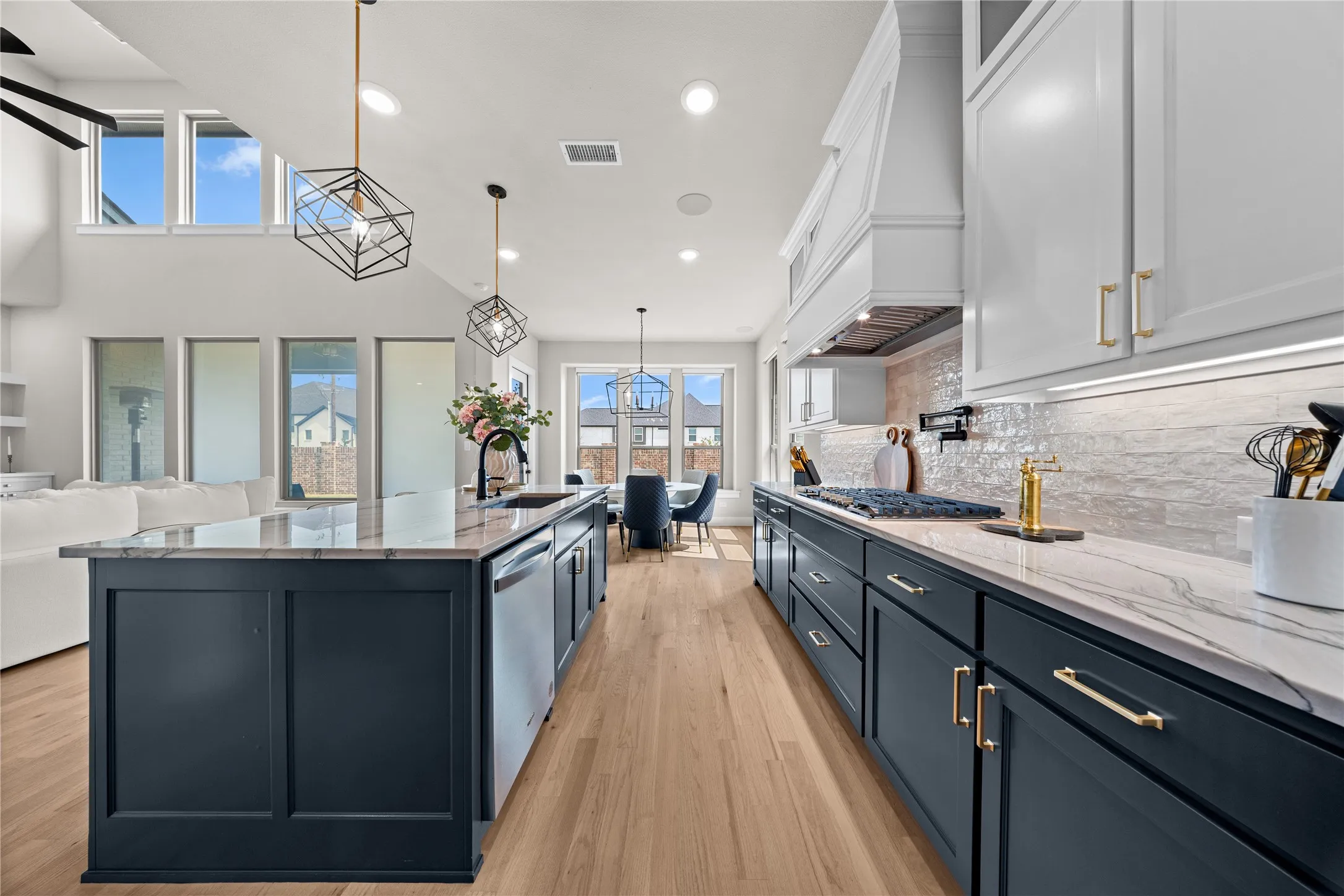 Gourmet kitchen featuring a large center island with waterfall-edge countertop, dual-zone cabinetry in navy and white finishes, stainless steel appliances, subway tile backsplash, wood-finish flooring, and abundant natural light from expansive windows and clerestory skylights overlooking the cityscape