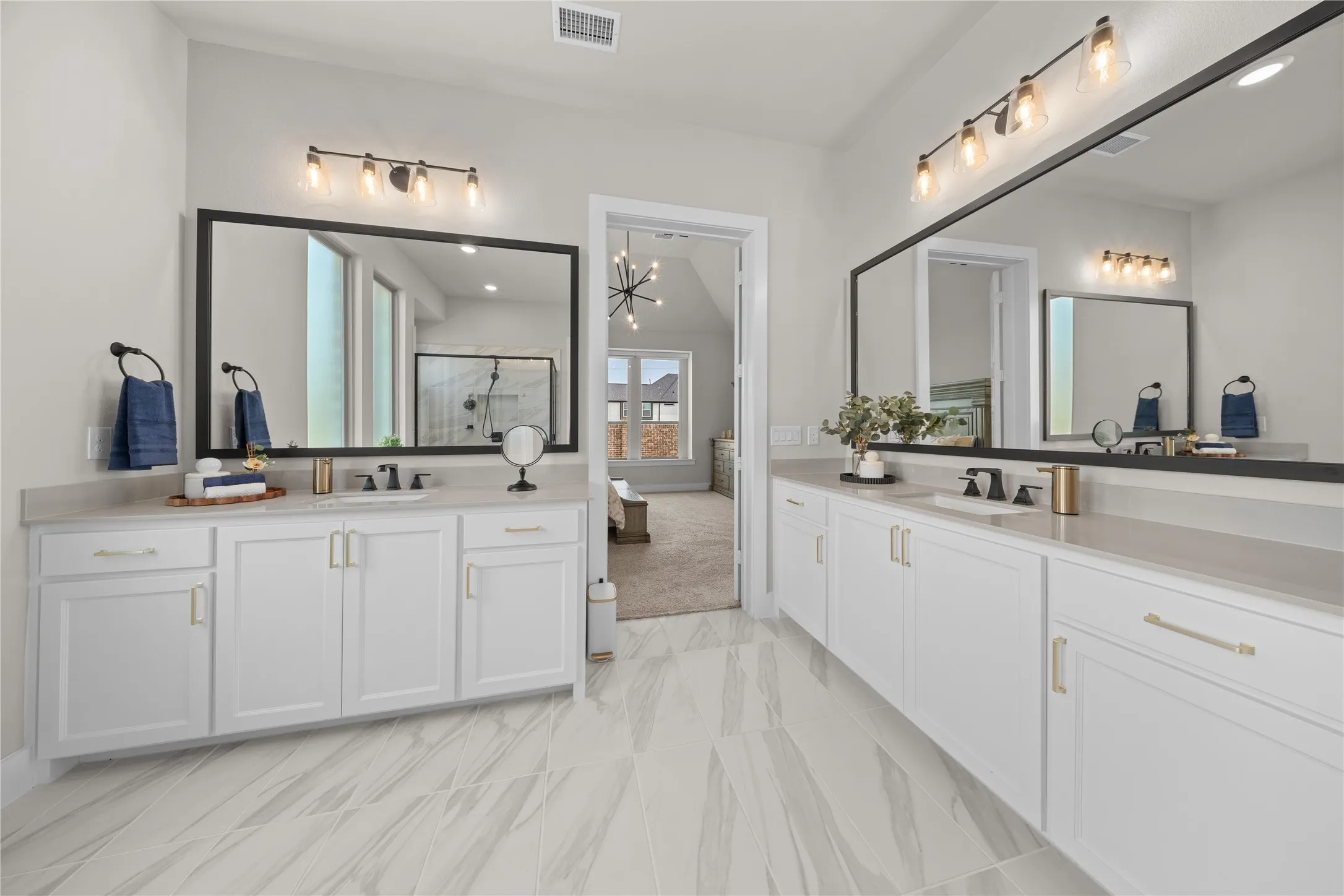 Dual white vanities with light-toned countertops and undermount sinks, complemented by matte black faucets and gold-toned hardware