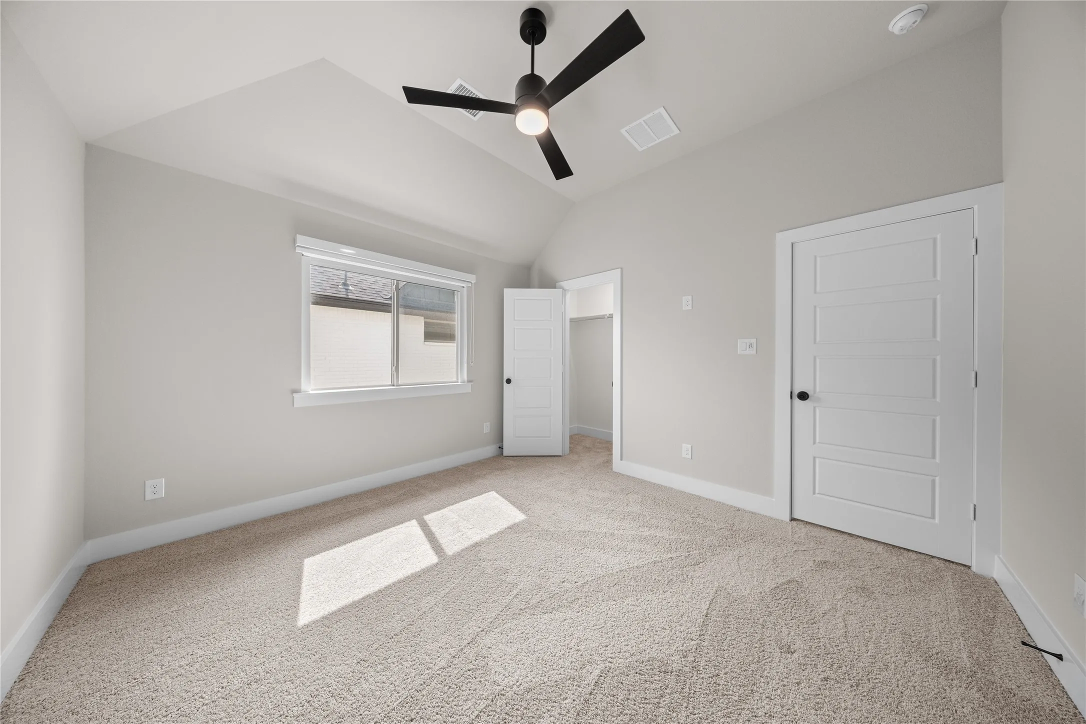 Bright and spacious bedroom featuring neutral carpeting, large window with natural light, ceiling fan with integrated lighting, and dual closet access with white panel doors