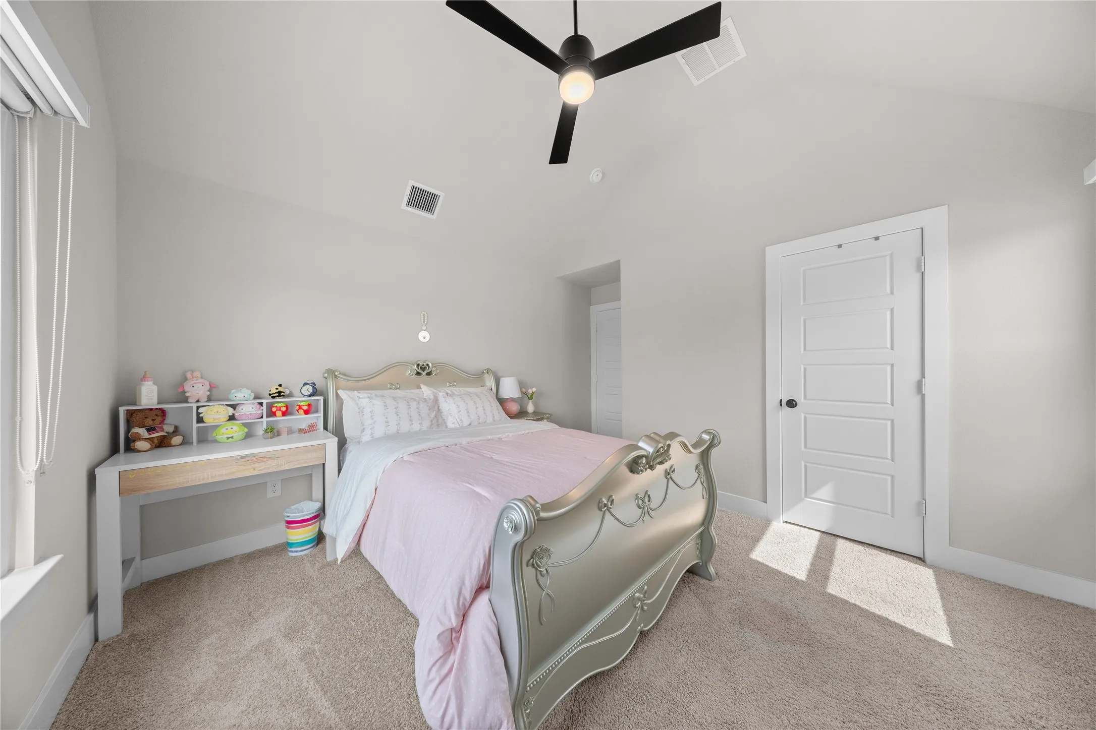 Bright secondary bedroom featuring soft natural light from large windows, carpeted flooring, a ceiling fan with integrated lighting, and convenient built-in shelving with storage​​‌​​​​‌​​‌‌​‌‌​​​‌‌​‌​‌​‌​​​‌​​ cubbies