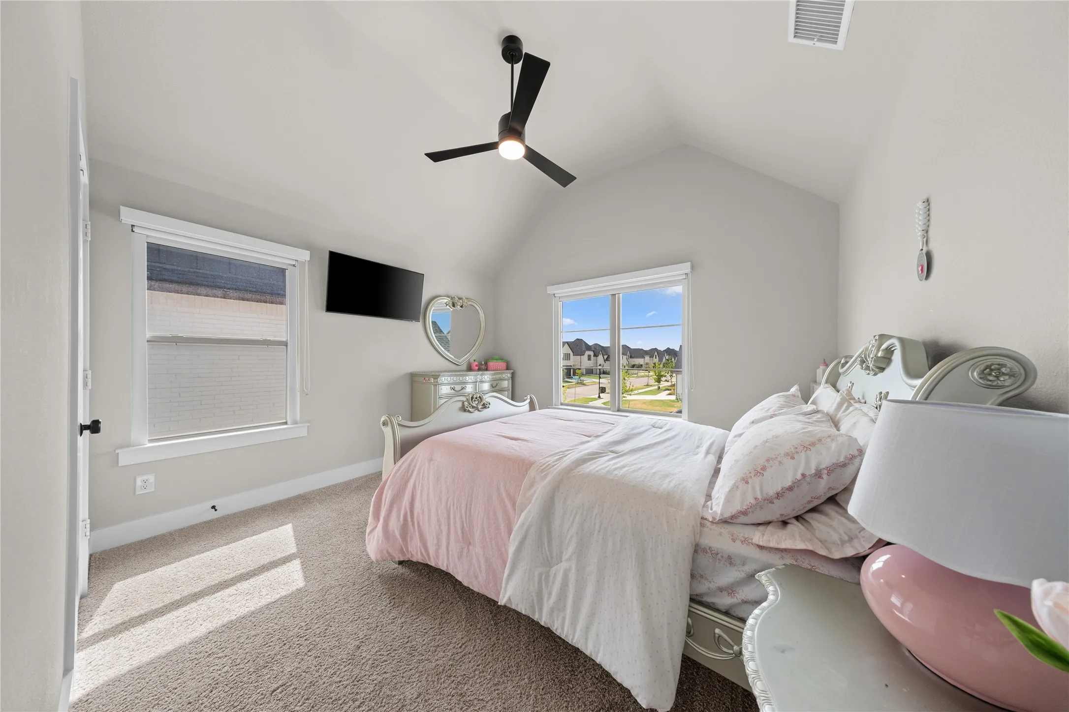 Vaulted ceiling with a black ceiling fan, two windows with white trim, light-colored carpeting, and light gray wall paint