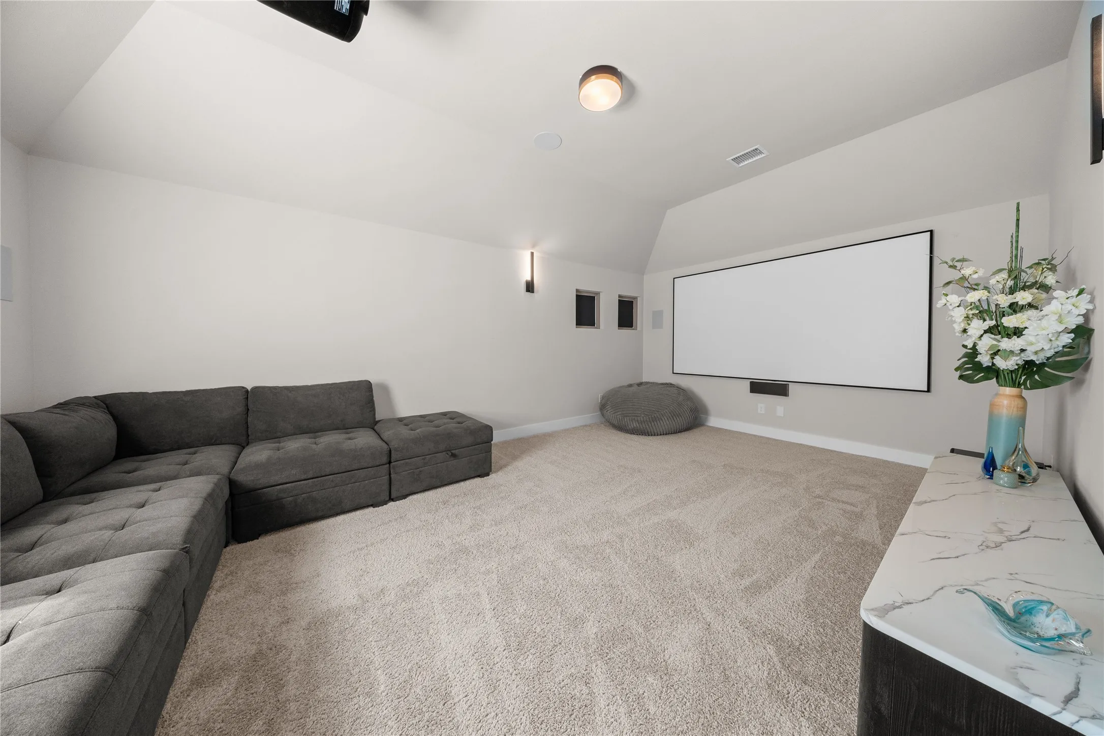Dedicated home theater room featuring a large projection screen, built-in surround sound speaker cutouts, recessed ceiling lighting, and comfortable sectional seating arrangement