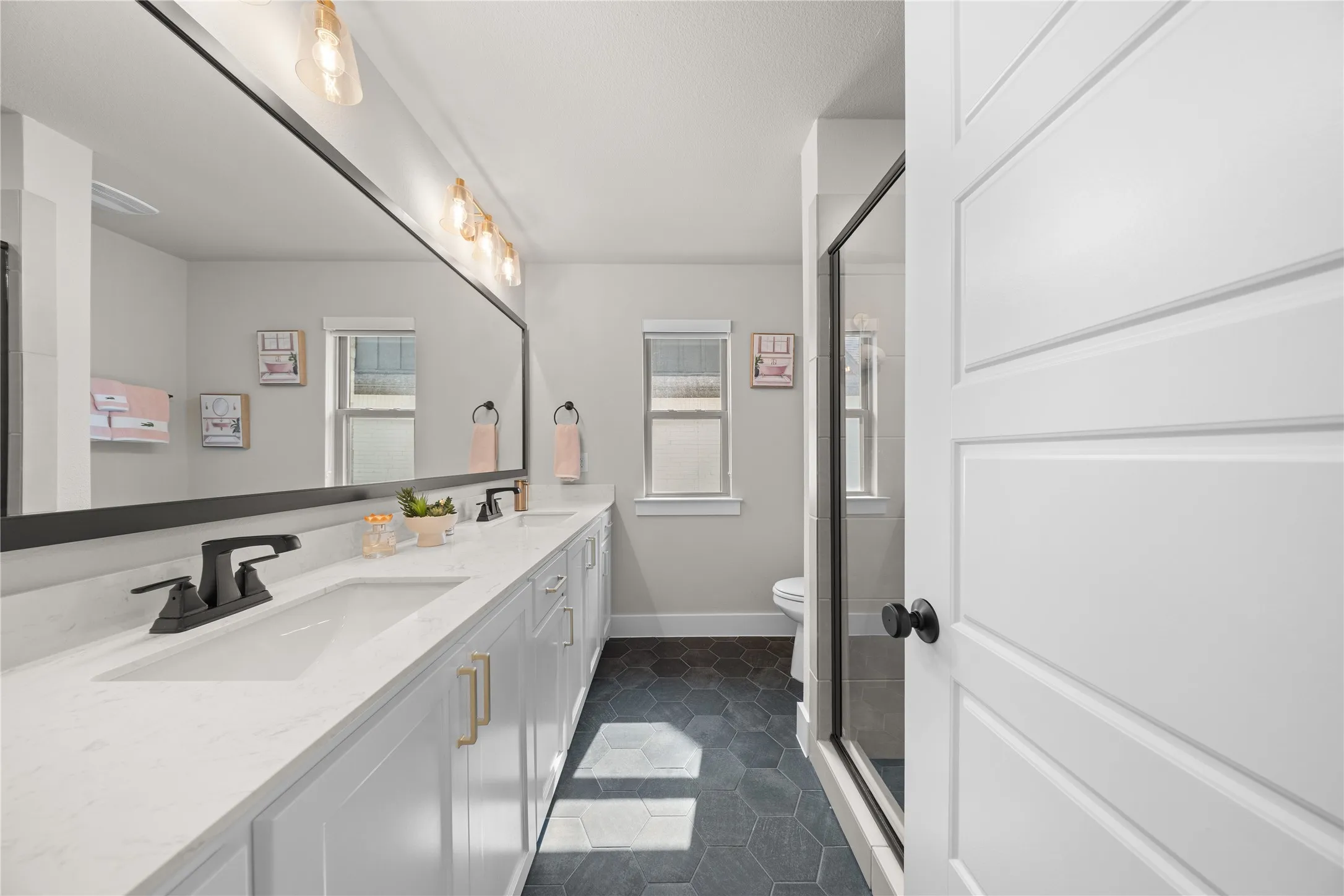 Spa-inspired primary bathroom featuring a dual-sink vanity with white cabinetry, quartz countertops, and matte black hardware