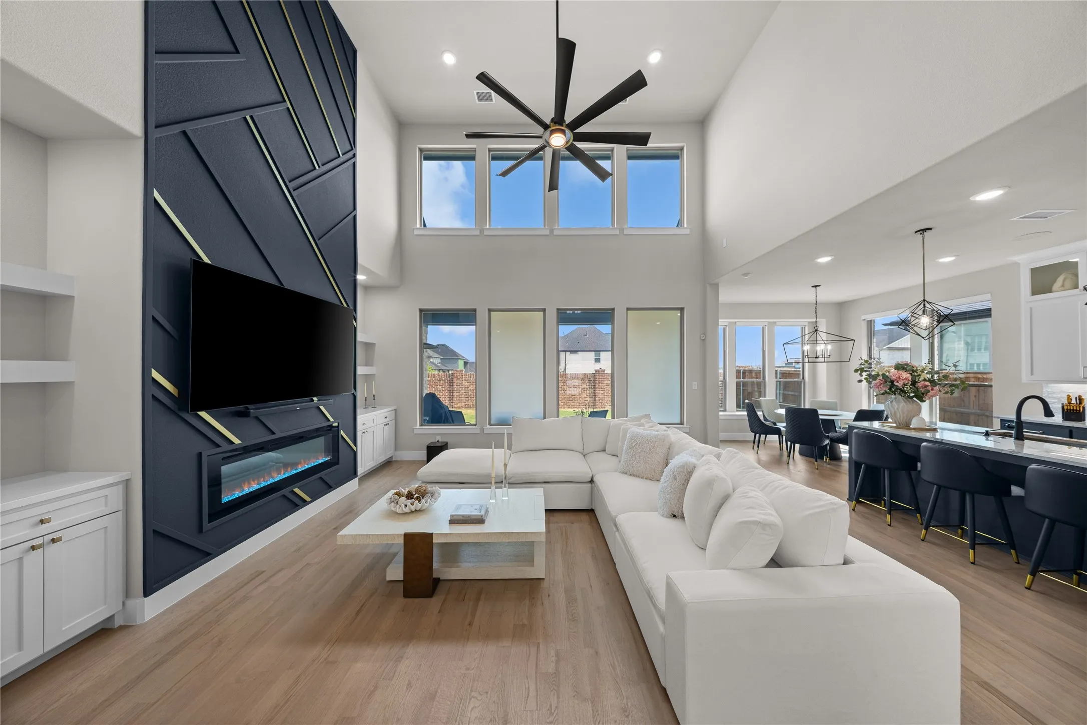 Contemporary open-concept living space featuring soaring ceilings with skylights, a linear gas fireplace with dark tile surround and built-in shelving, wide-plank wood-finish flooring, and expansive windows framing mountain backdrop