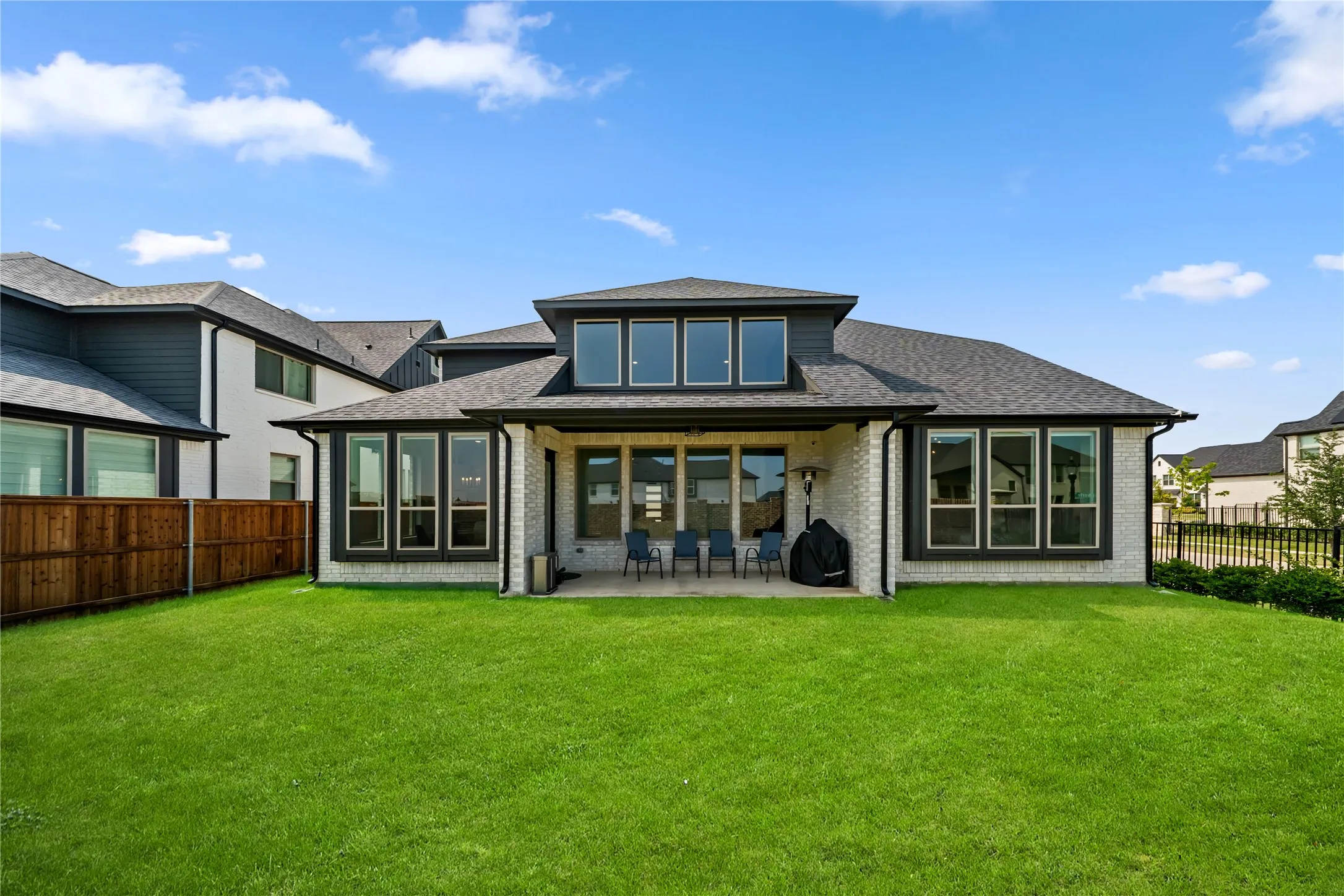 Expansive green lawn with a covered patio featuring a brick exterior and multiple large windows