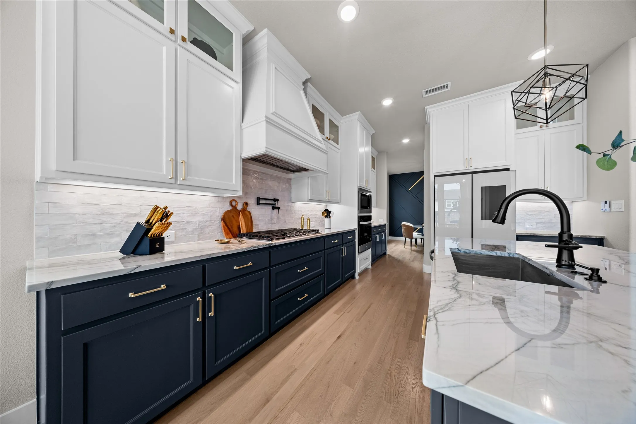Stunning chef's kitchen featuring white shaker cabinetry with glass-front uppers, navy lower cabinets with brushed gold hardware, and a marble-look quartz island countertop
