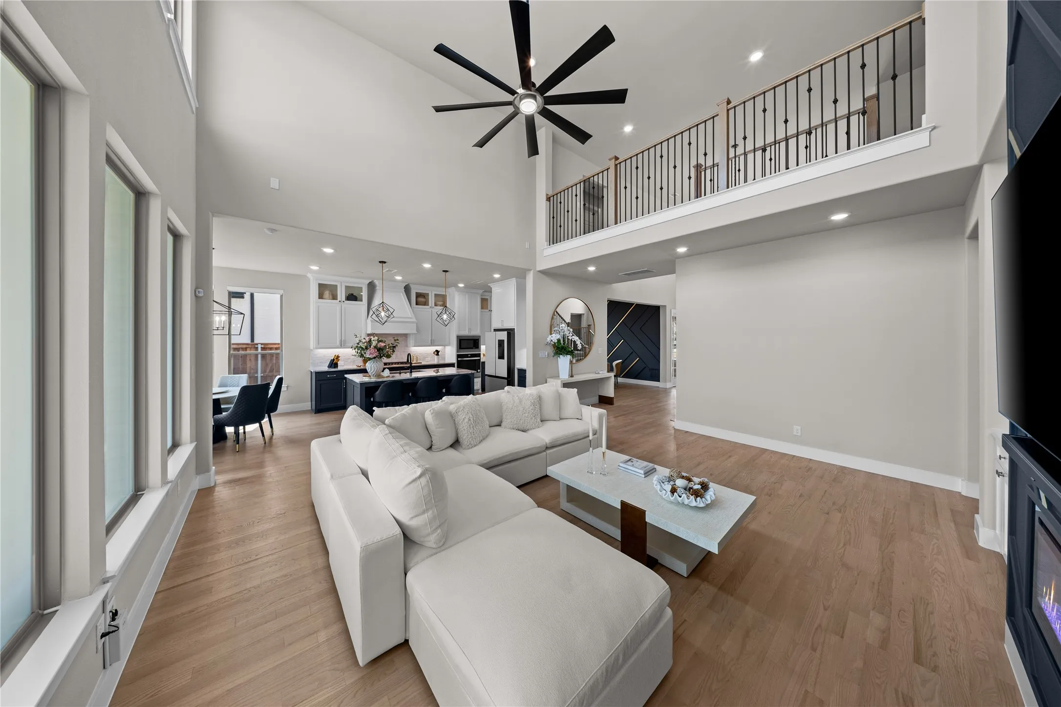 Open-concept living space featuring soaring vaulted ceilings with a modern ceiling fan, abundant natural light from expansive windows, wood-finish flooring throughout, and a generously proportioned seating area