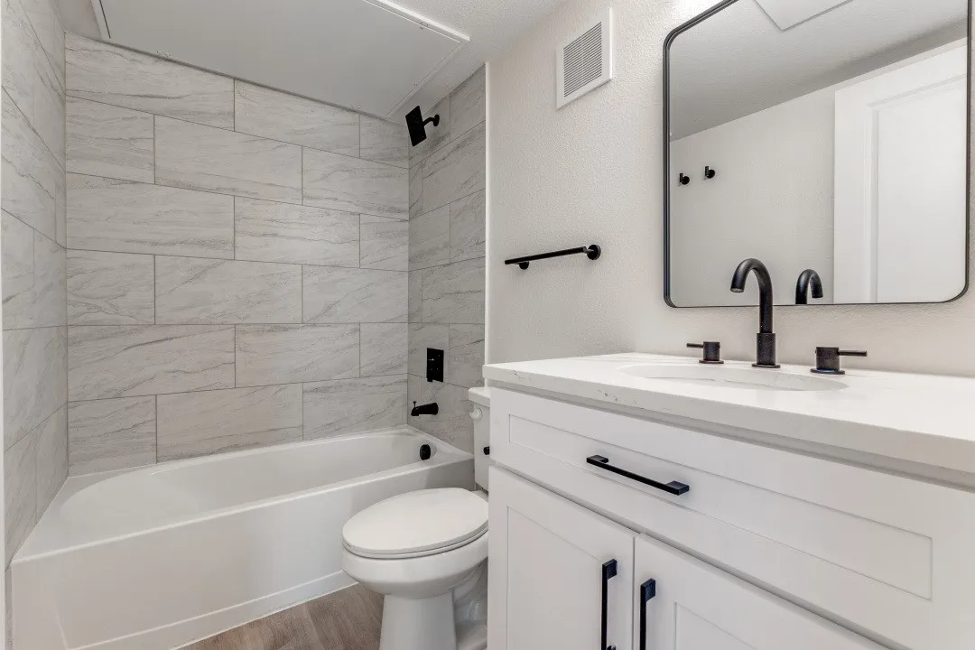 Bathroom featuring a white vanity with a light-toned countertop, a black-framed mirror, and a white tub with light-toned tiled walls