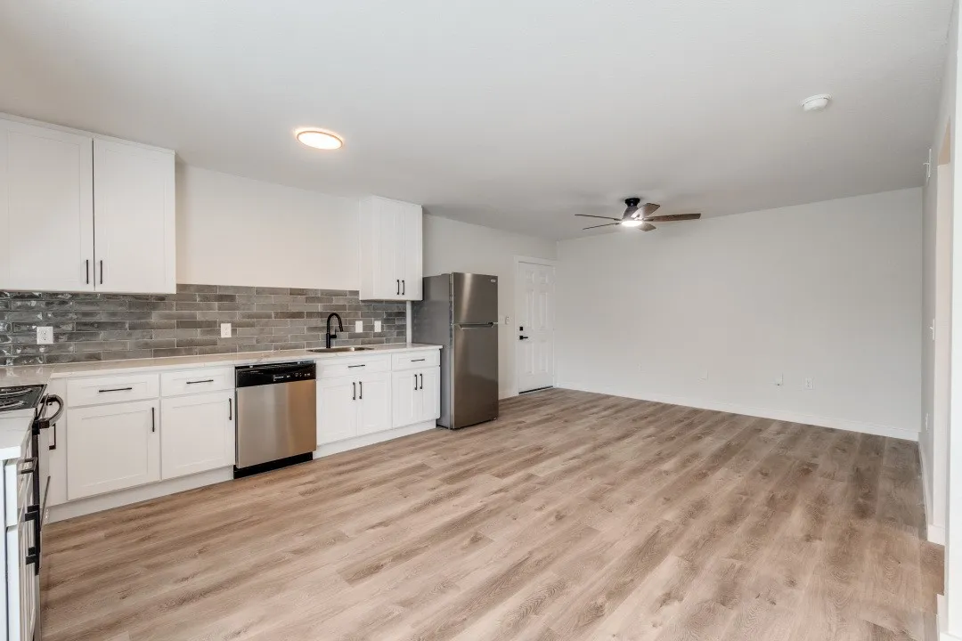 Modern kitchen with white cabinetry, stainless steel appliances, a grey subway tile backsplash, and light wood-finish flooring