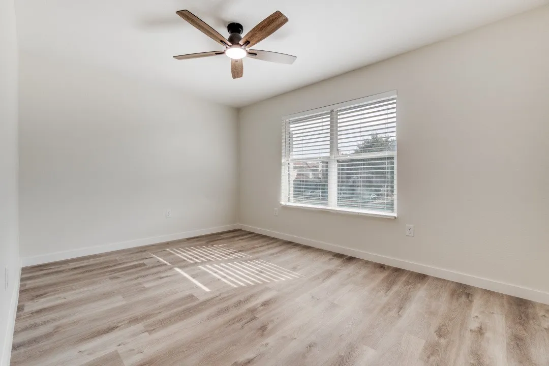 Spacious room featuring wood-finish flooring, a large window with blinds, and a ceiling fan with integrated lighting