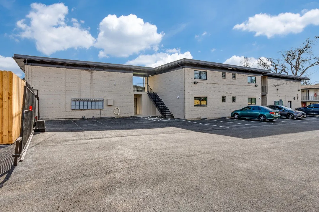 Off-street parking lot with ample space, featuring a perimeter fence and direct access to the building's exterior stairwells and mailboxes