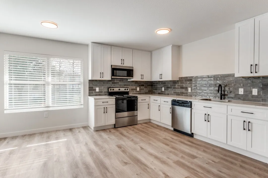 Contemporary kitchen featuring white cabinetry, stainless steel appliances, a dark subway tile backsplash, light wood-finish flooring, and ample natural light from a large window