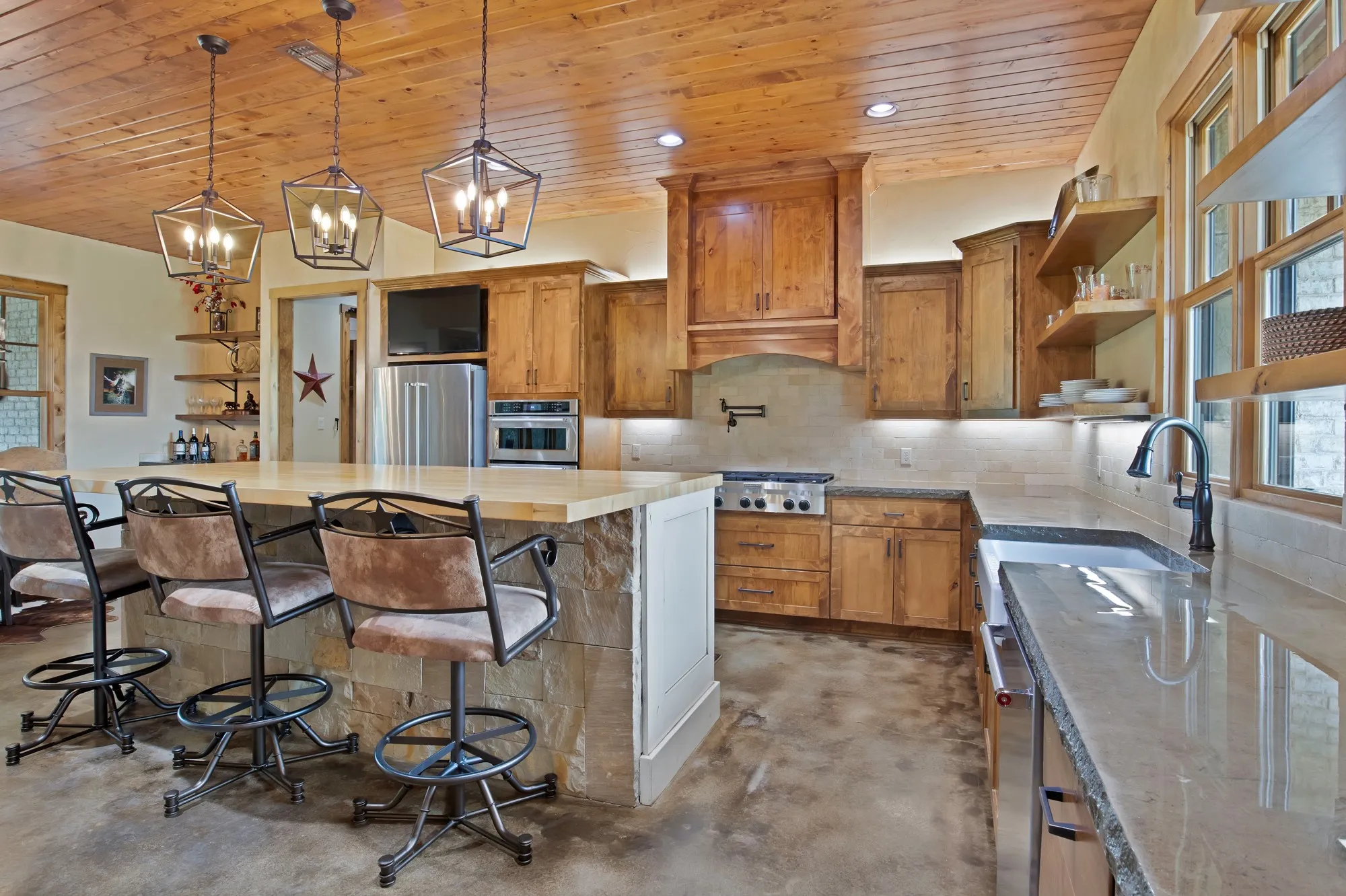 Kitchen featuring a stone-clad island with a light-toned countertop, wood-finish ceiling, and exposed wood cabinetry
