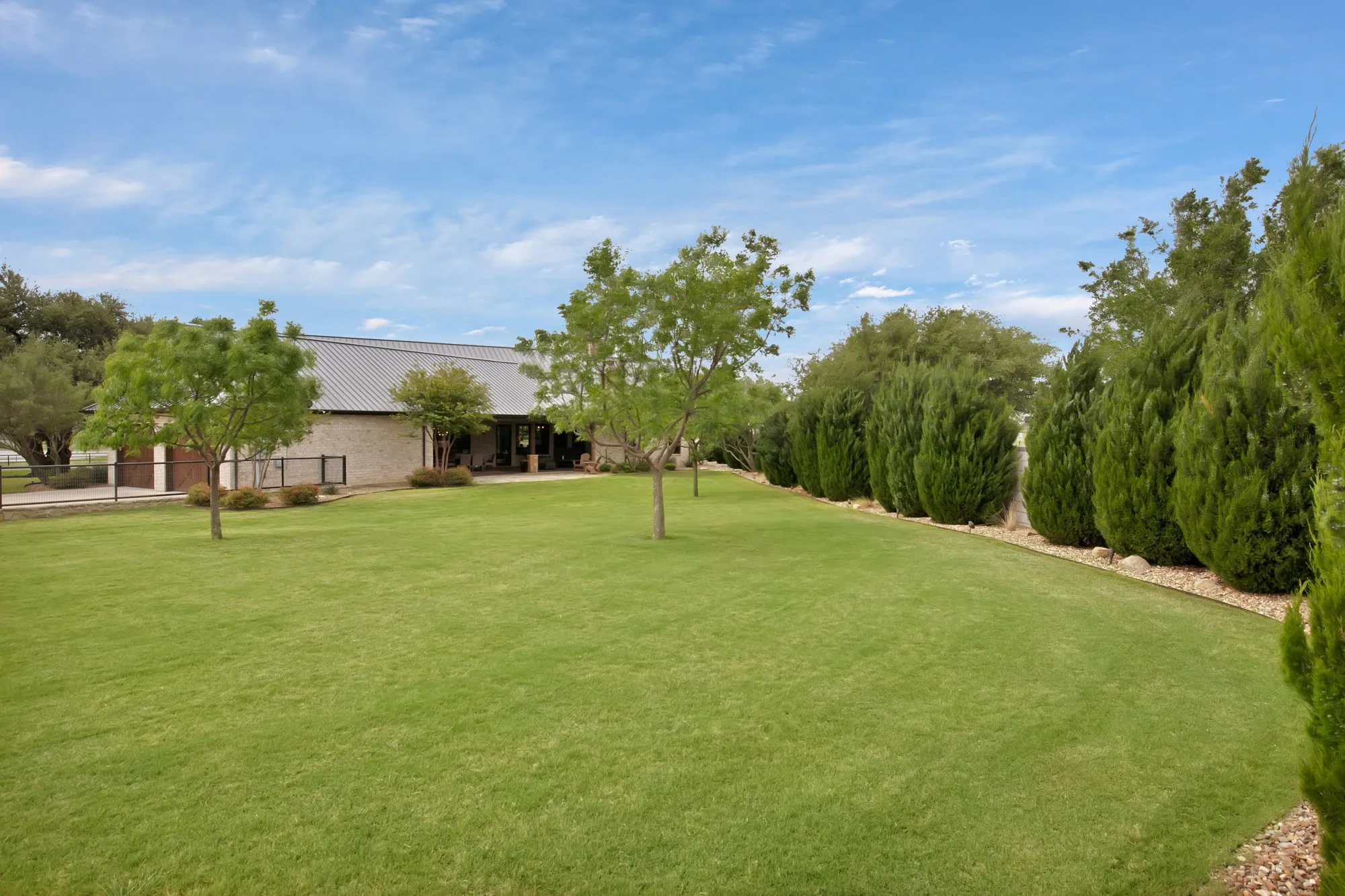Expansive green lawn with mature trees and a structured hedge row