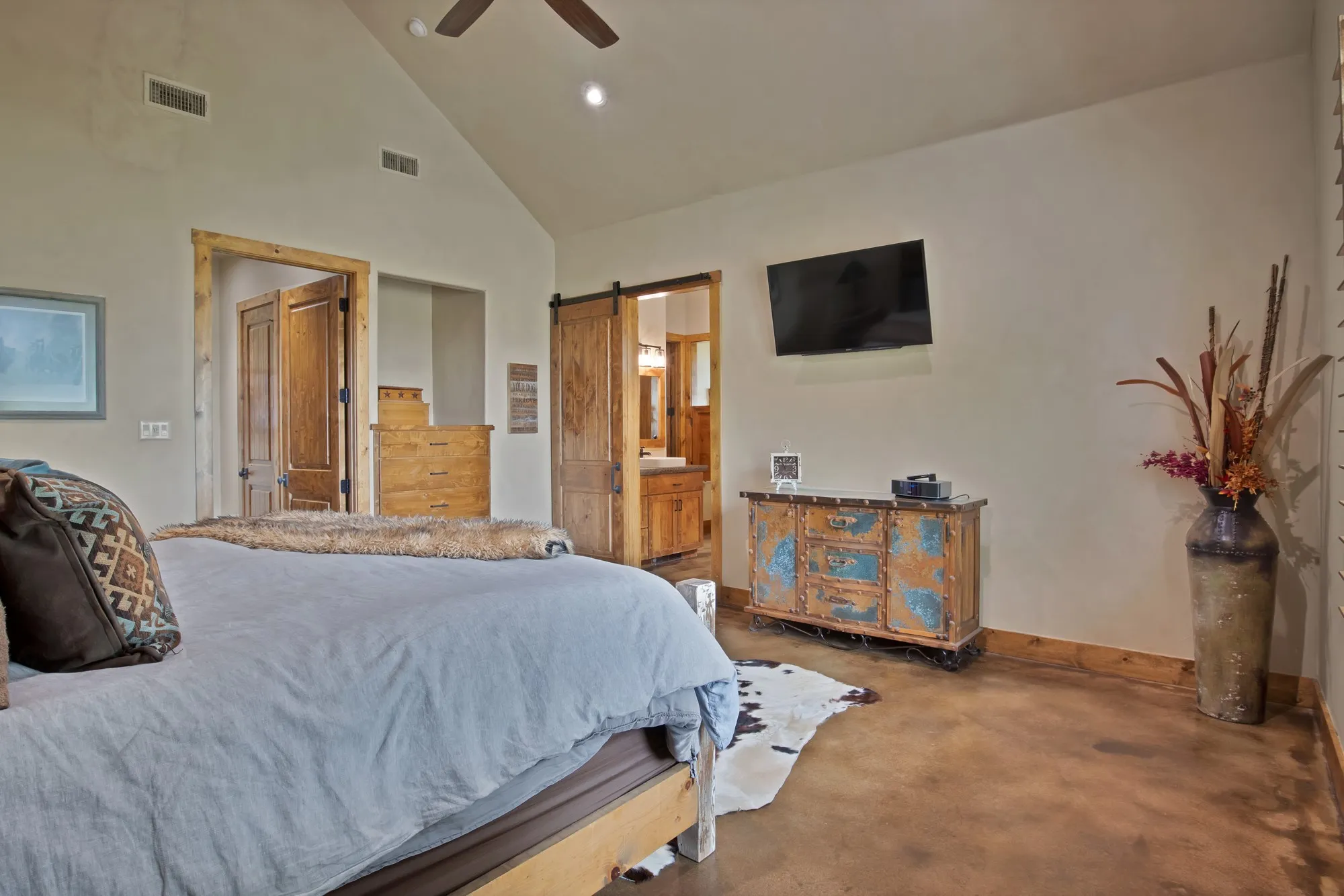Vaulted ceiling with a ceiling fan, stained concrete flooring, wood trim, and wood barn door entry to a bathroom