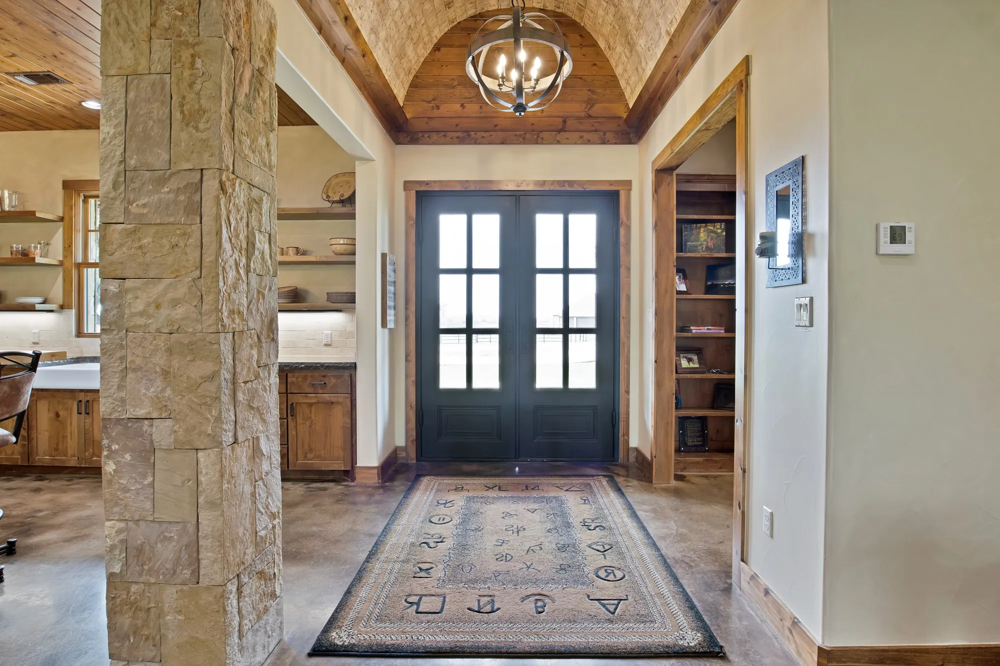 Entryway featuring a barrel-vaulted wood-paneled ceiling with an iron chandelier, double glass-paneled entry doors, and a stone-clad column