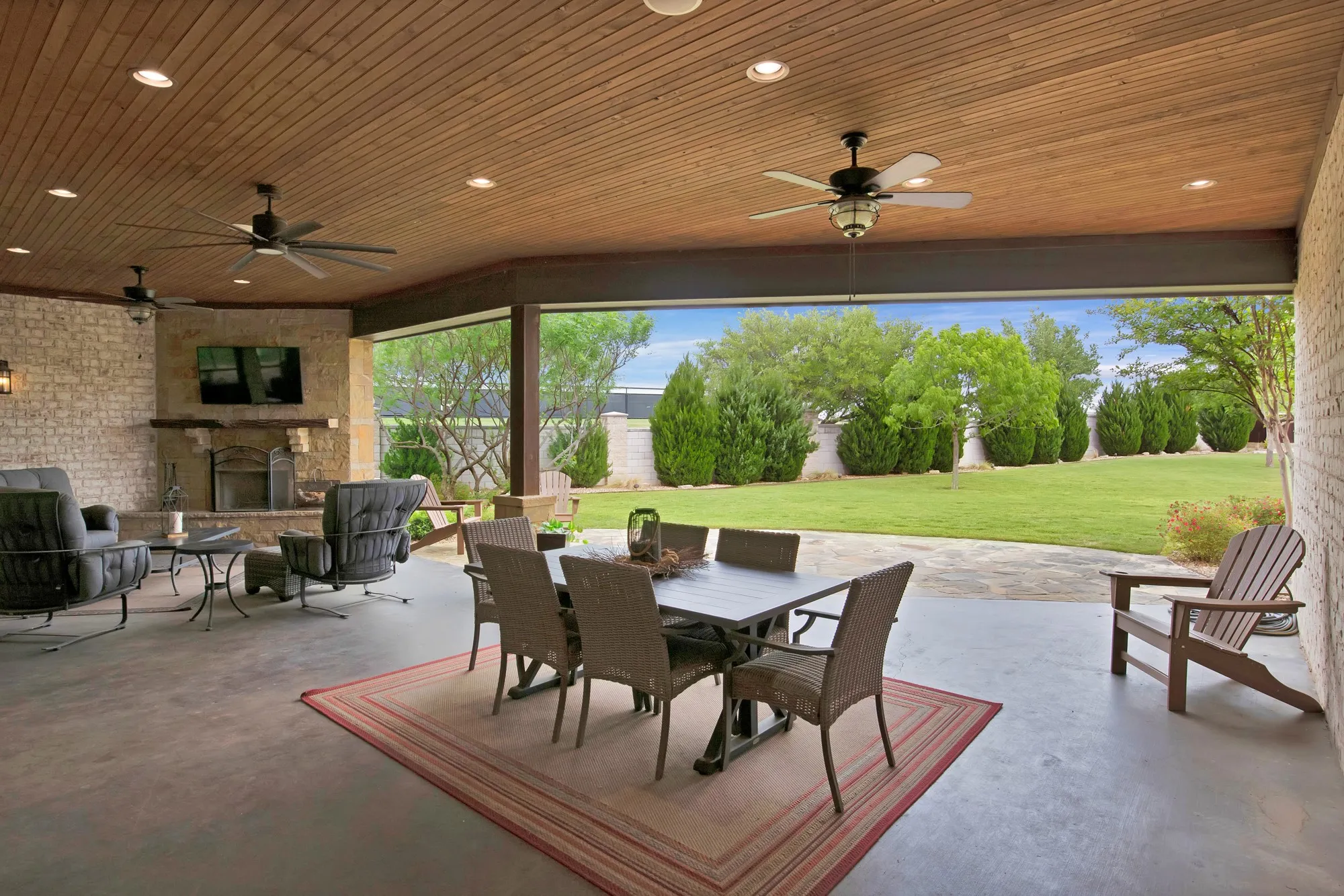Spacious covered patio featuring a stone-clad fireplace and wood-finish ceiling with recessed lighting