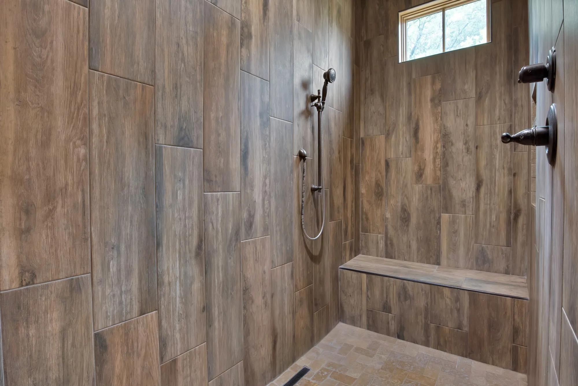 Walk-in shower featuring wood-look tile walls, an integrated shower bench, a handheld shower fixture, and oil-rubbed bronze hardware