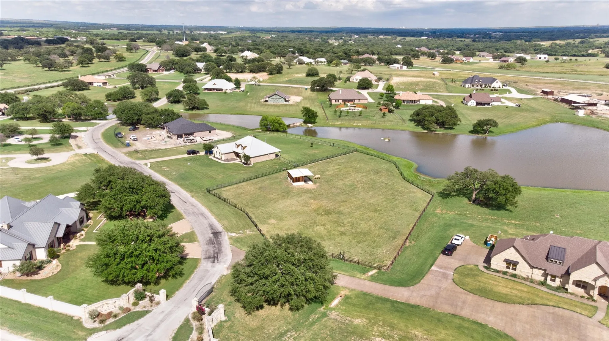 Aerial view showcasing expansive acreage with mature landscaping, multiple residences and outbuildings, paved driveway circulation, and a private pond feature