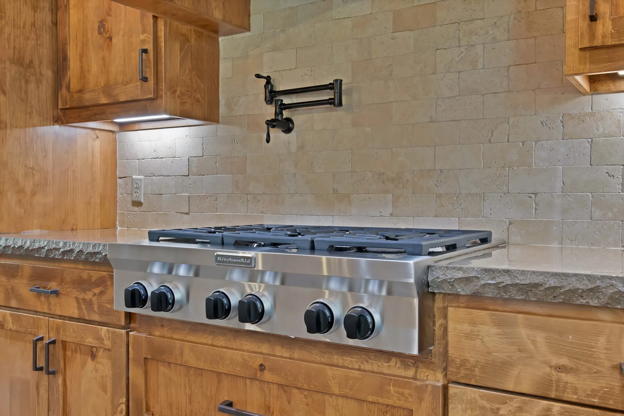 Stainless steel professional-grade gas range with a pot filler, set against a stacked stone backsplash