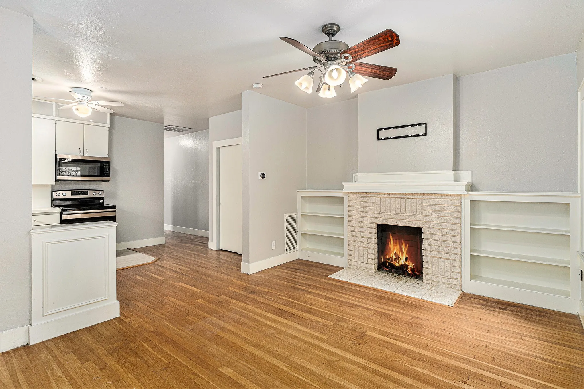 Unfurnished living room with ceiling fan, a brick fireplace, and light hardwood / wood-style floors