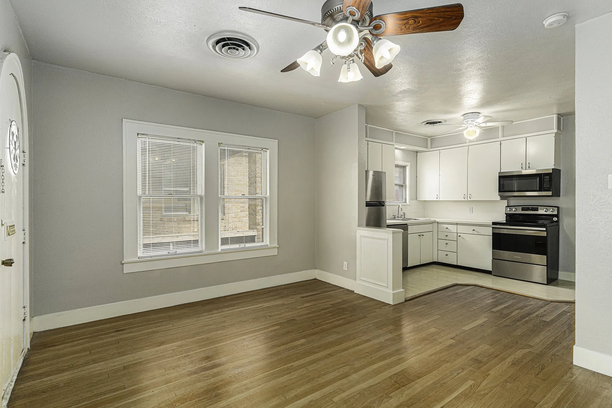 Kitchen with appliances with stainless steel finishes, ceiling fan, wood-type flooring, and white cabinetry
