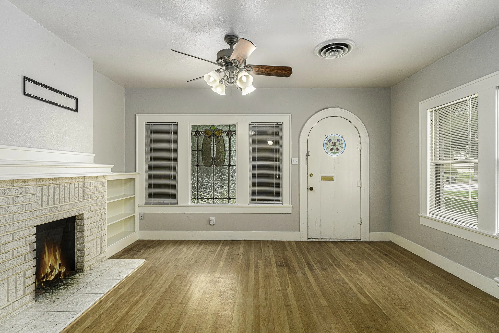 Unfurnished living room with built in features, a brick fireplace, hardwood / wood-style floors, and ceiling​​‌​​​​‌​​‌‌​‌‌​​​‌‌​‌​‌​‌​​​‌​​ fan
