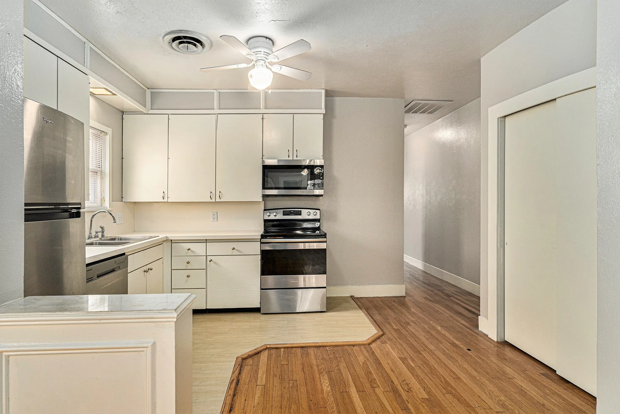 Kitchen with ceiling fan, stainless steel appliances, white cabinets, light wood-type flooring, and sink